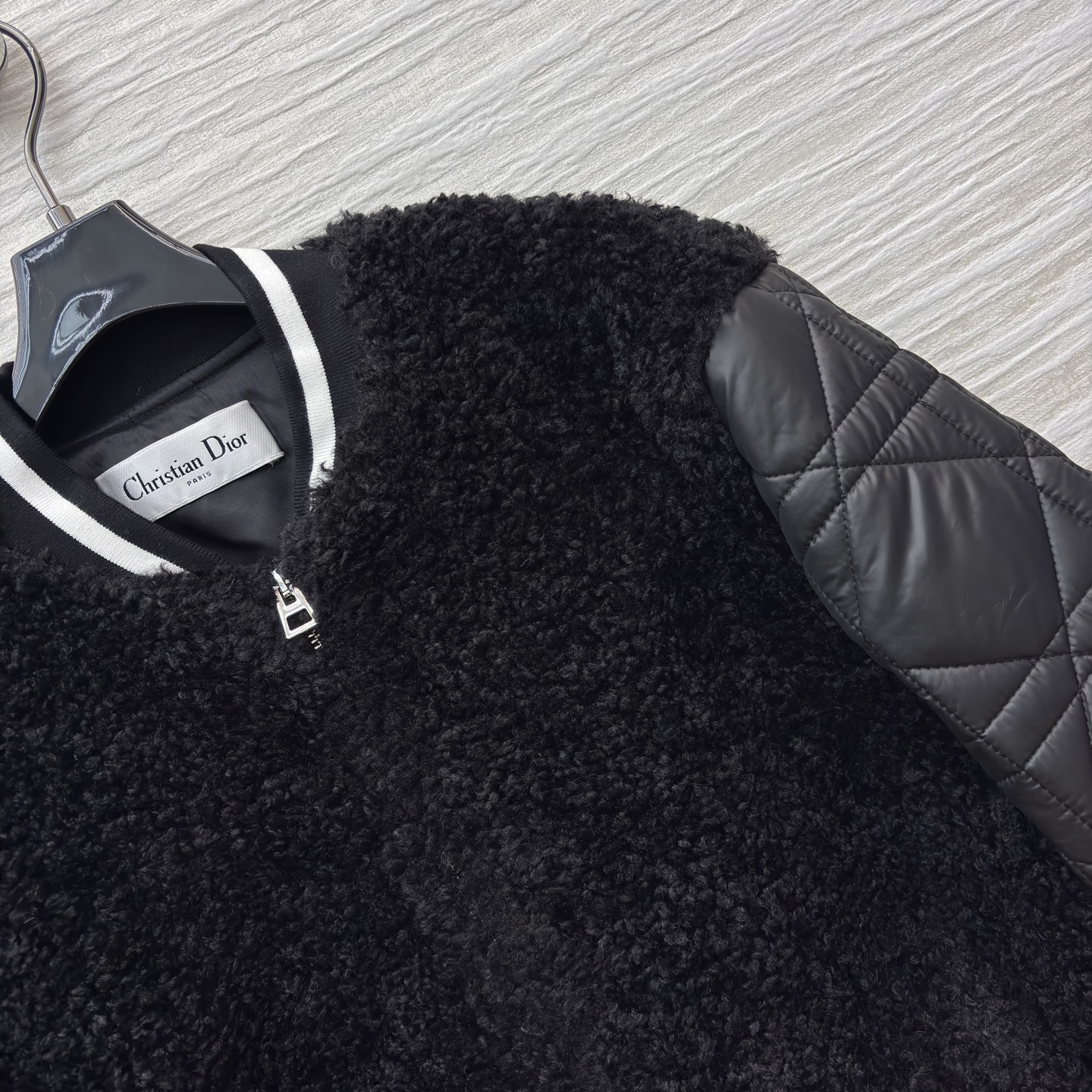 D家棒球夹克 是酷飒与温暖的完美融合 黑色毛绒主体柔软蓬松 菱格绗缝皮袖利落有型 经典黑白条纹饰边点缀细