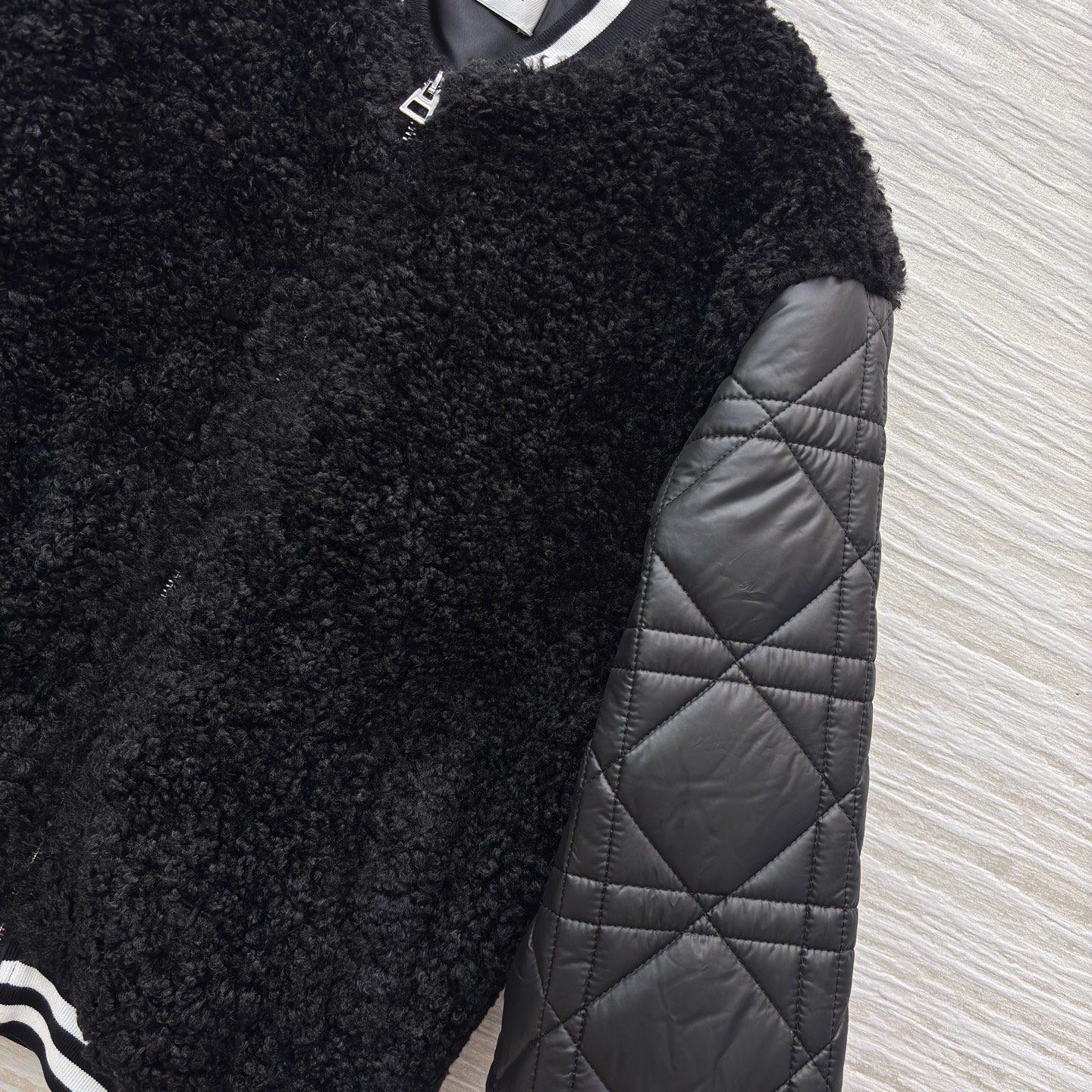 D家棒球夹克 是酷飒与温暖的完美融合 黑色毛绒主体柔软蓬松 菱格绗缝皮袖利落有型 经典黑白条纹饰边点缀细