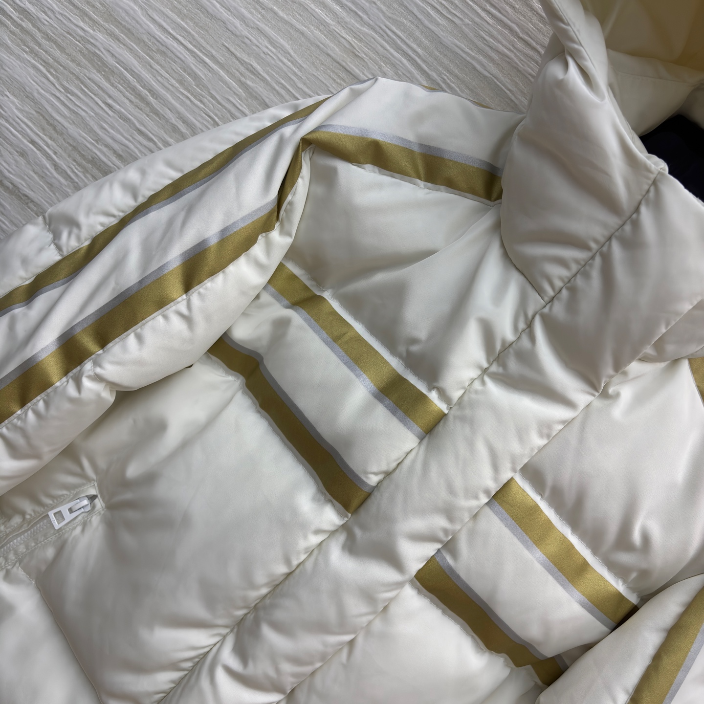 D家 撞色连帽羽绒服 是冬日里的温柔铠甲 米白底色衬出干净氛围 金调条纹与侧边装饰点亮细节 连帽设计裹紧
