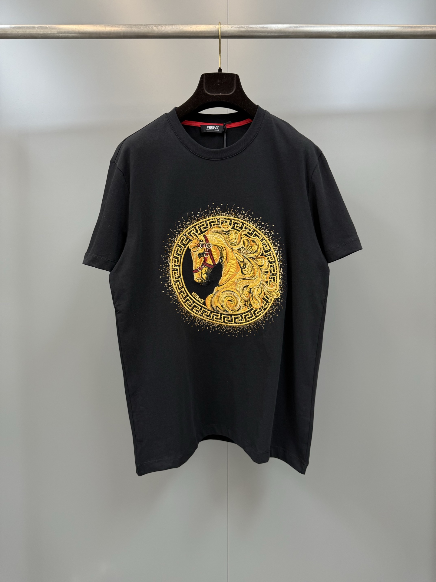 NO:780486,Versace 26ss Year of the Horse limited embroidered short sleeves  The 'hanging shirt' specially designed for the New Year combines the brand's classic elements with the zodiac culture, which has great visual impact and symbolic meaning. The classic bottom shirt is paired with bright golden embroidery, full of high-end feeling, and comes with a 'noble buff'. It is suitable for daily wear and festival wear. On the front of the gilt horse totem is a three-dimensional golden horse head with floating mane.  Elegance, exquisite details, symbolizing 'perseverance leads to immediate success', in line with the enterprising meaning of the New Year. The horse's head is surrounded by the brand's iconic Greek key pattern, and the outer ring is decorated with hot diamonds/sequins to enhance the sense of luxury. It is Versace's iconic design language. There are 'VERSACE' letters below the horse's head, and there is a brand label on the inner collar. The details highlight the authenticity.  Suitable for New Year's parties and festivals, it means 'get rich immediately', 'success immediately', and seek good luck; Versace-clothing,versace,versace,T-shirt,19860909Versace 26ss马年限定刺绣短袖 专为新年设计的“开挂战衣”,融合了品牌经典元素与生肖文化,极具视觉冲击力和象征意义.经典底衫搭配璀璨金色刺绣,高级感拉满,自带“贵气buff”,日常穿炸场,节日穿应景.鎏金骏马图腾正面是立体感十足的金色骏马头像,鬃毛飘逸,细节精致,象征“一往无前、马到成功”,契合新年进取寓意.马头被品牌标志性的希腊回纹环绕,外圈点缀烫钻/亮片,提升奢华感,是范思哲标志性设计语言.马头下方有“VERSACE”字母,内领口有品牌标签,细节处彰显正品身份. 适合新年聚会、节日穿搭,寓意“马上暴富”“马到成功”,讨个好彩头；,范思哲-服装,versace,versace,T-shirt,,Women's clothing