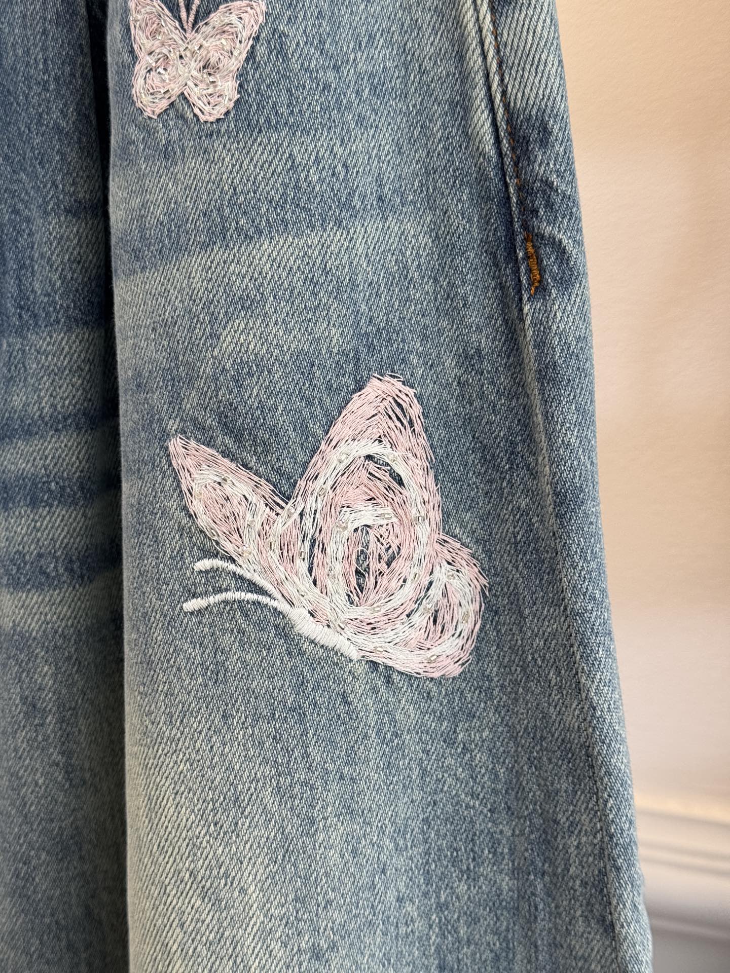 Ann Andel**蝴蝶刺绣弯刀牛仔裤融合轻奢设计与休闲丹宁风格的单品，以复古水洗丹宁为基底，搭配精致