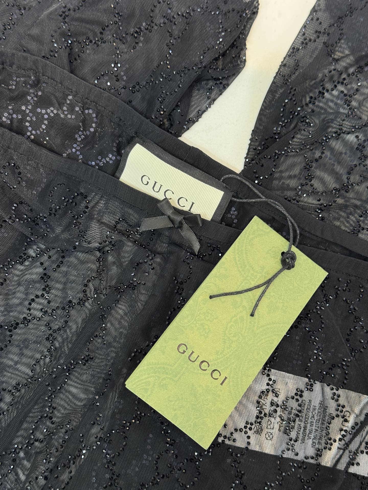 gucc* 饰GG仿水晶薄纱蕾丝紧身裤外层为深棕色蕾丝透视长裤，带有双G暗纹与烫钻点缀，裤脚处的双G烫钻