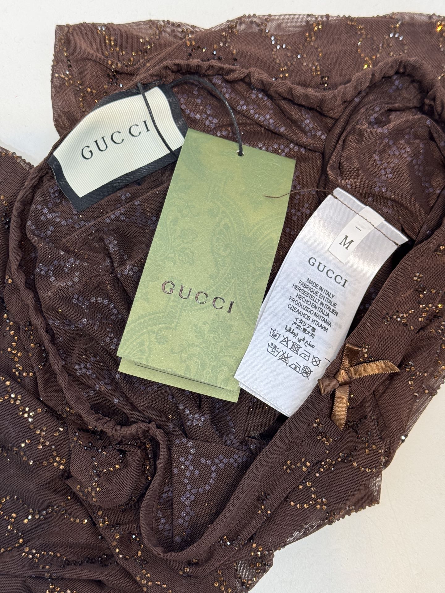 gucc* 饰GG仿水晶薄纱蕾丝紧身裤外层为深棕色蕾丝透视长裤，带有双G暗纹与烫钻点缀，裤脚处的双G烫钻