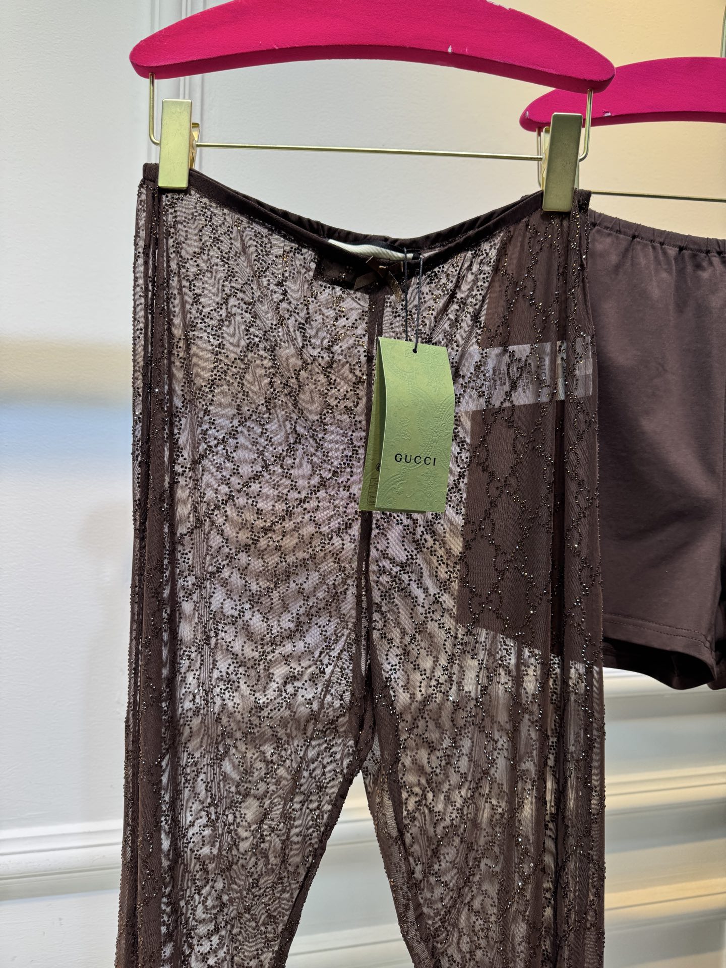 gucc* 饰GG仿水晶薄纱蕾丝紧身裤外层为深棕色蕾丝透视长裤，带有双G暗纹与烫钻点缀，裤脚处的双G烫钻