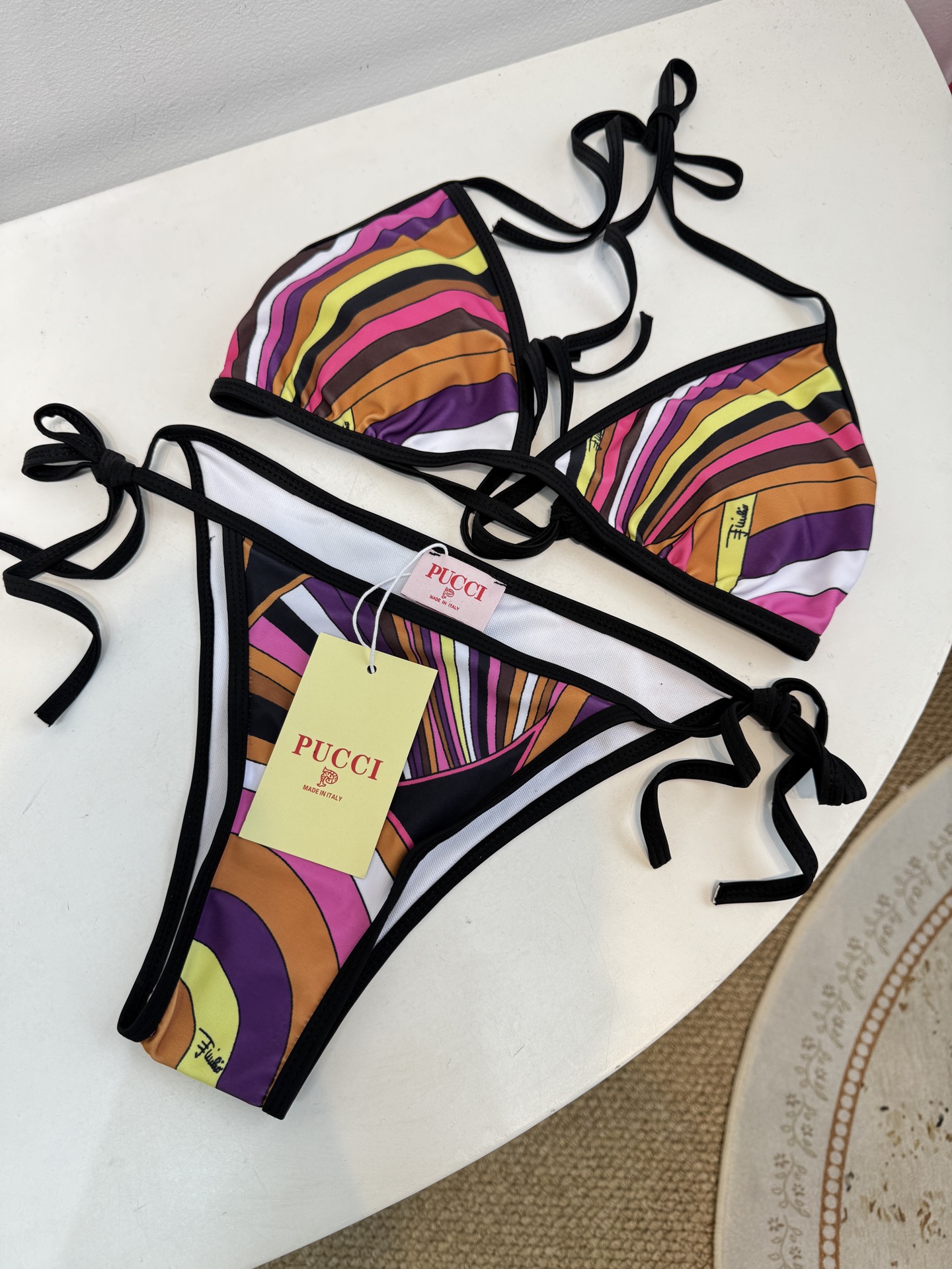 Pucci 三角杯系带比基尼泳衣采用经典的几何条纹印花，融合了粉、紫、棕、黄等高饱和度色彩，呈现出品牌标