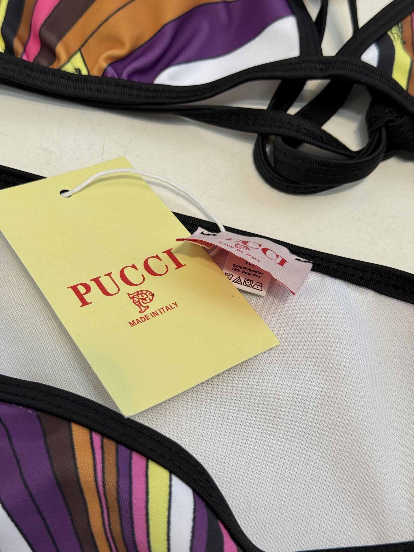 Pucci 三角杯系带比基尼泳衣采用经典的几何条纹印花，融合了粉、紫、棕、黄等高饱和度色彩，呈现出品牌标
