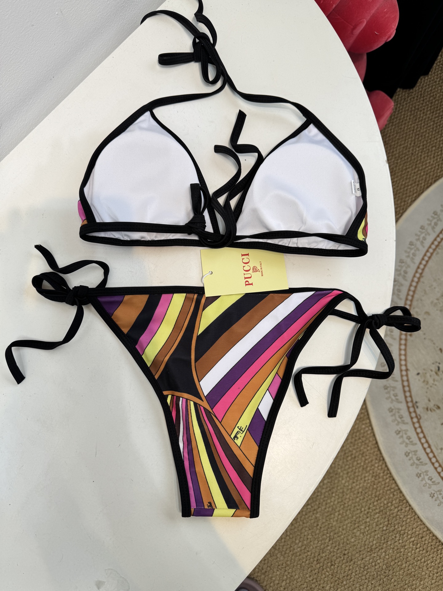 Pucci 三角杯系带比基尼泳衣采用经典的几何条纹印花，融合了粉、紫、棕、黄等高饱和度色彩，呈现出品牌标