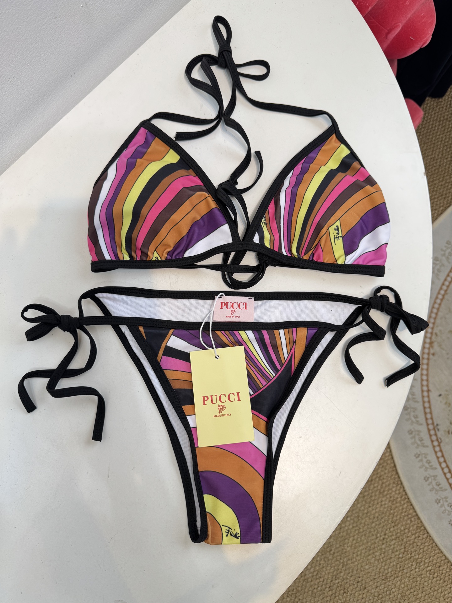 Pucci 三角杯系带比基尼泳衣采用经典的几何条纹印花，融合了粉、紫、棕、黄等高饱和度色彩，呈现出品牌标
