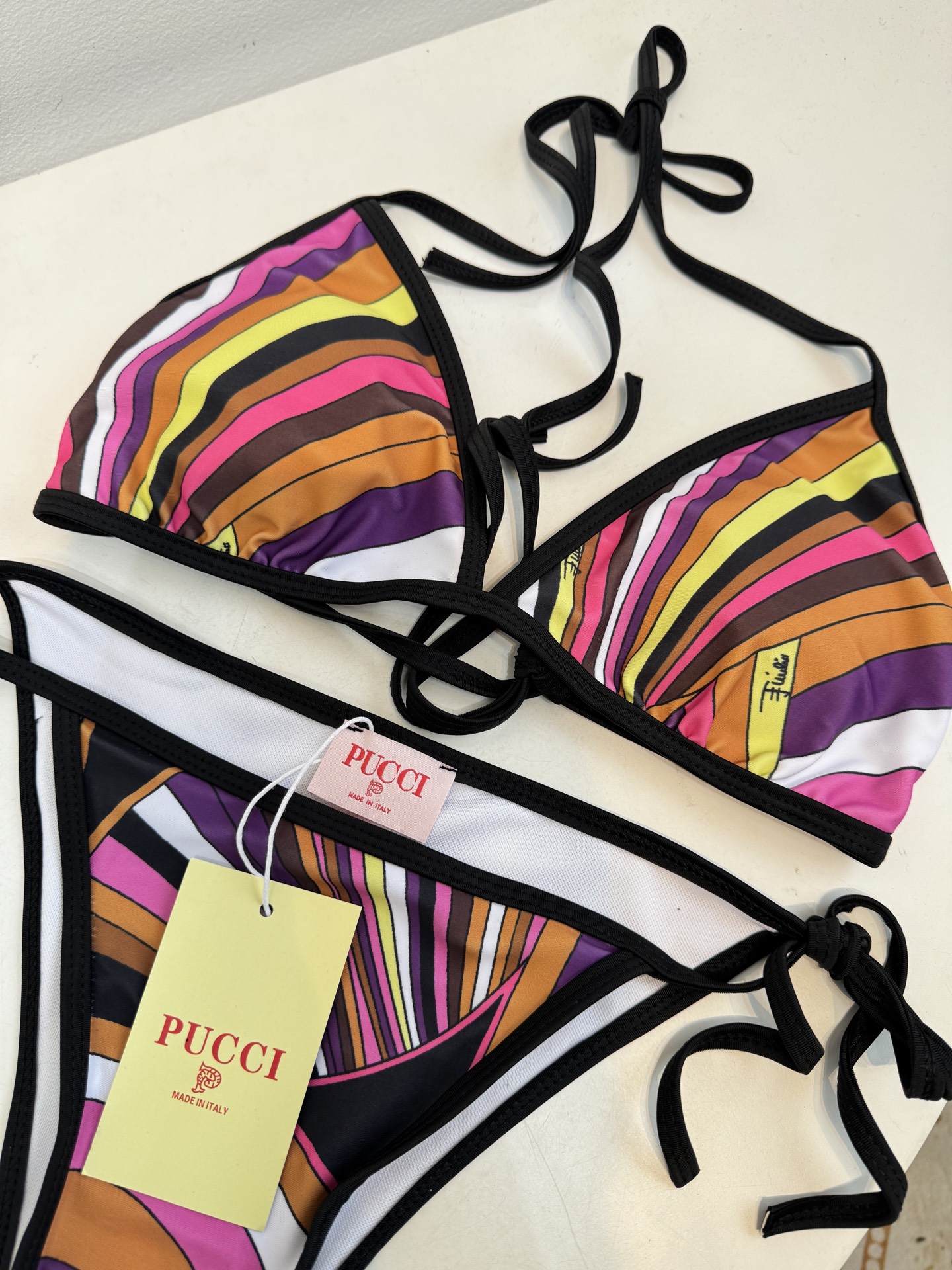 Pucci 三角杯系带比基尼泳衣采用经典的几何条纹印花，融合了粉、紫、棕、黄等高饱和度色彩，呈现出品牌标