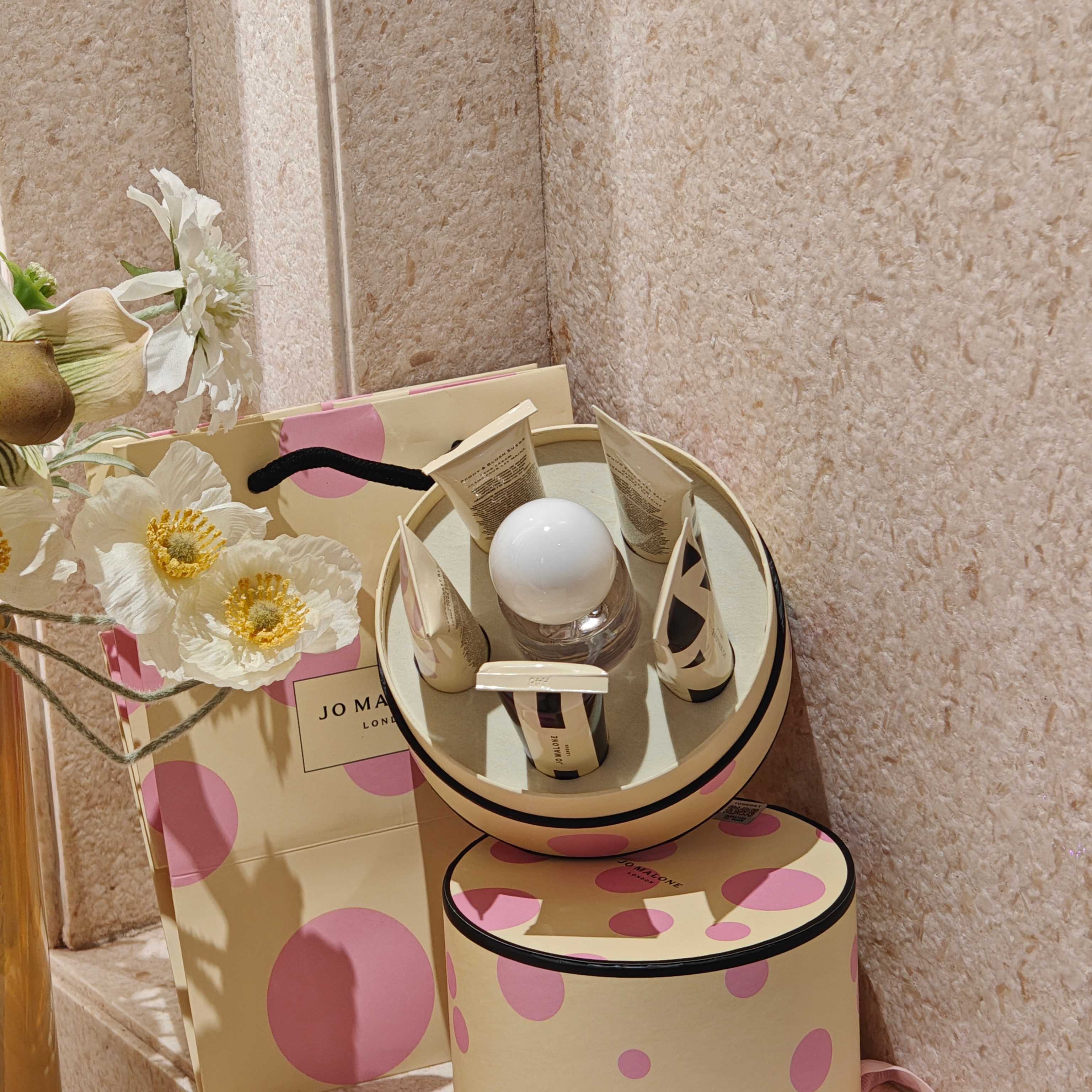 NO:879349,Jo Malone Sakura Limited Edition 1-to-5 Gift Box | A Set for Fragrance Lovers. The stunning pink polka dot round box gift box has a creamy yellow background with soft pink polka dots. The ribbon bow is gentle and romantic. It is matched with a handbag of the same series. The gift-giving has a high-end atmosphere, and the unboxing ceremony directly fills the air.  The set contains a 30ml limited-edition cherry blossom eau de toilette with a transparent round bottle cap and a sweet and soft cherry blossom aroma, clean, gentle and not sweet. It is paired with five 30ml limited-edition geometric print hand creams, including five popular fragrances: blue wind chime, English pear, sage sea salt, peony and cherry blossom, each with a healing aroma.  The texture of the hand cream is smooth and easy to absorb. It is refreshing after application and does not stick to the phone. It can be reapplied daily and has a long-lasting fragrance on your fingertips. The fragrance of the eau de toilette is clear and natural, suitable for commuting and dating. A set of perfume + five popular hand creams, taking into account the fragrance experience and hand care. For personal use, you can change the fragrance every day to unlock different atmospheres. It is also very thoughtful as a birthday and holiday souvenir. The packaging is exquisite and the fragrance is complete. Whether it is given to a girlfriend or a female friend, it is a romantic choice.19860909祖玛珑樱花限定一拖五礼盒｜香氛爱好者本命套组  颜值封神的粉波点圆盒礼盒,奶黄底色搭配柔粉圆点,丝带蝴蝶结温柔烂漫,配套同系列手提袋,送礼自带高级氛围感,开箱仪式感直接拉满.  套装内含30ml樱花限定淡香水,通透圆球瓶盖,清甜柔和的樱花香气,干净温柔不甜腻；搭配五支30ml限定几何印花护手霜,囊括蓝风铃、英国梨、鼠尾草海盐、牡丹、樱花五大热门香调,一支一种治愈香气.  护手霜质地顺滑好吸收,涂完清爽不粘手机,日常随身补涂,指尖持久留香；淡香水留香清透自然,通勤、约会都适配.一套集齐香水+五款人气手霜,兼顾香氛体验与手部护理.  自用可每日换香,解锁不同氛围感；作为生日、节日伴手礼也格外走心,包装精致、香调齐全,不管送闺蜜还是女生朋友,都是不出错的浪漫选择.,香水护手霜,accessory