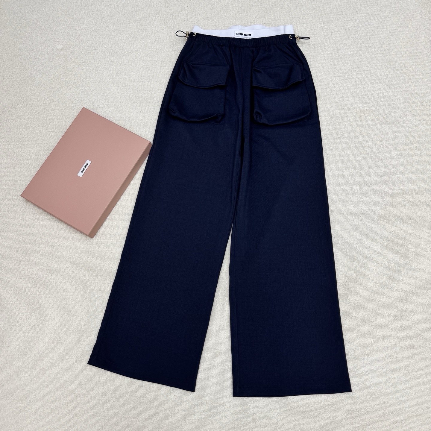 NO:807852,miumi*26Ss new spring and summer style contrasting letter threaded waist patchwork overalls丨Exclusive high-end version!  The iconic white-edged contrasting waistband brightens up the whole, and the two-tone navy blue and light khaki colors suit a variety of spring styles. Made of crisp and drapey cotton blended fabric, the front panel is independently cut and spliced with large pockets to design a cool workwear style with loose wide legs and a lazy and relaxed feel. The three-dimensional pleat design on the trousers enhances the functional attributes of the workwear, and the drawstring waistband is comfortable.  Style and style. It can be paired with a short waistless top to create an American hot girl style, or layered with a loose sweatshirt to create a casual street feel. It is a core item in the summer wardrobe that is both recognizable and practical. Two colors are available in stock, S/M/L, real shot details,, miumiu, hoodie, sweatshirts,19860909miumi*26Ss春夏新款 撞色字母螺纹腰拼接工装裤丨独家高版出品！以标志性的白边撞色腰头点亮整体,藏蓝色与浅卡其双色调适配多元春日风格.采用挺括垂坠的棉质混纺面料,前片独立剪栽拼接大口袋设计工装酷酷宽松阔腿自带慵懒松弛感,裤身立体褶裥设计强化工装机能属性,抽绳腰头兼顾舒适度与造型感.可搭配短款露腰上衣打造美式辣妹风,或叠穿宽松卫衣营造随性街头感,是夏季衣橱里兼具辨识度与实穿性的核心单品.两色现货发售S/M/L实拍细节图,,miumiu,hoodie,sweatshirts,,Women's clothing