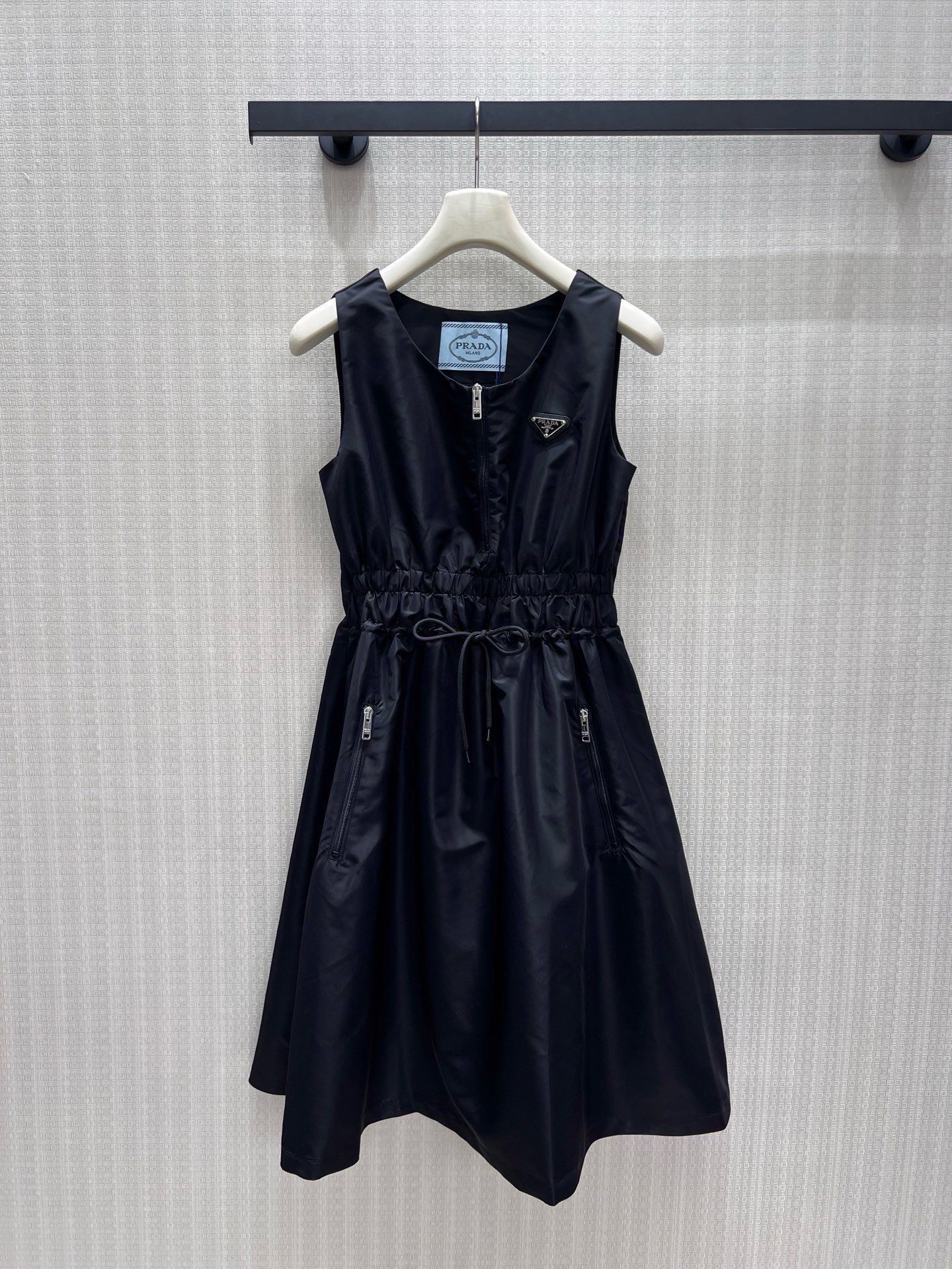 NO:952483,26 new spring and summer dresses  Pra**'s iconic regenerated nylon outlines neat lines, and the matte texture has high-level tension. The V-neck half-open zipper and drawstring waist design balance the coolness and soft curves of workwear, and the A-line skirt is light and gives off a casual aura. The metal triangle logo is embellished with side pocket zipper details, which combines sports genes and light luxury style. It interprets the effortless fashion attitude of urban women. Ready-made smL real shot details, prada, skirts,1986090926春夏新品 连衣裙 Pra**标志性再生尼龙勾勒利落线条,哑光质感自带高级张力.V领半开拉链与抽绳收腰设计,平衡工装飒爽与柔媚曲线,A字裙摆轻扬间尽释随性气场.金属三角徽标点缀,搭配侧袋拉链细节,将运动基因与轻奢格调精妙融合,演绎都市女性不费力的时髦态度.现货出售smL实拍细节图,,prada,skirts,,Women's clothing