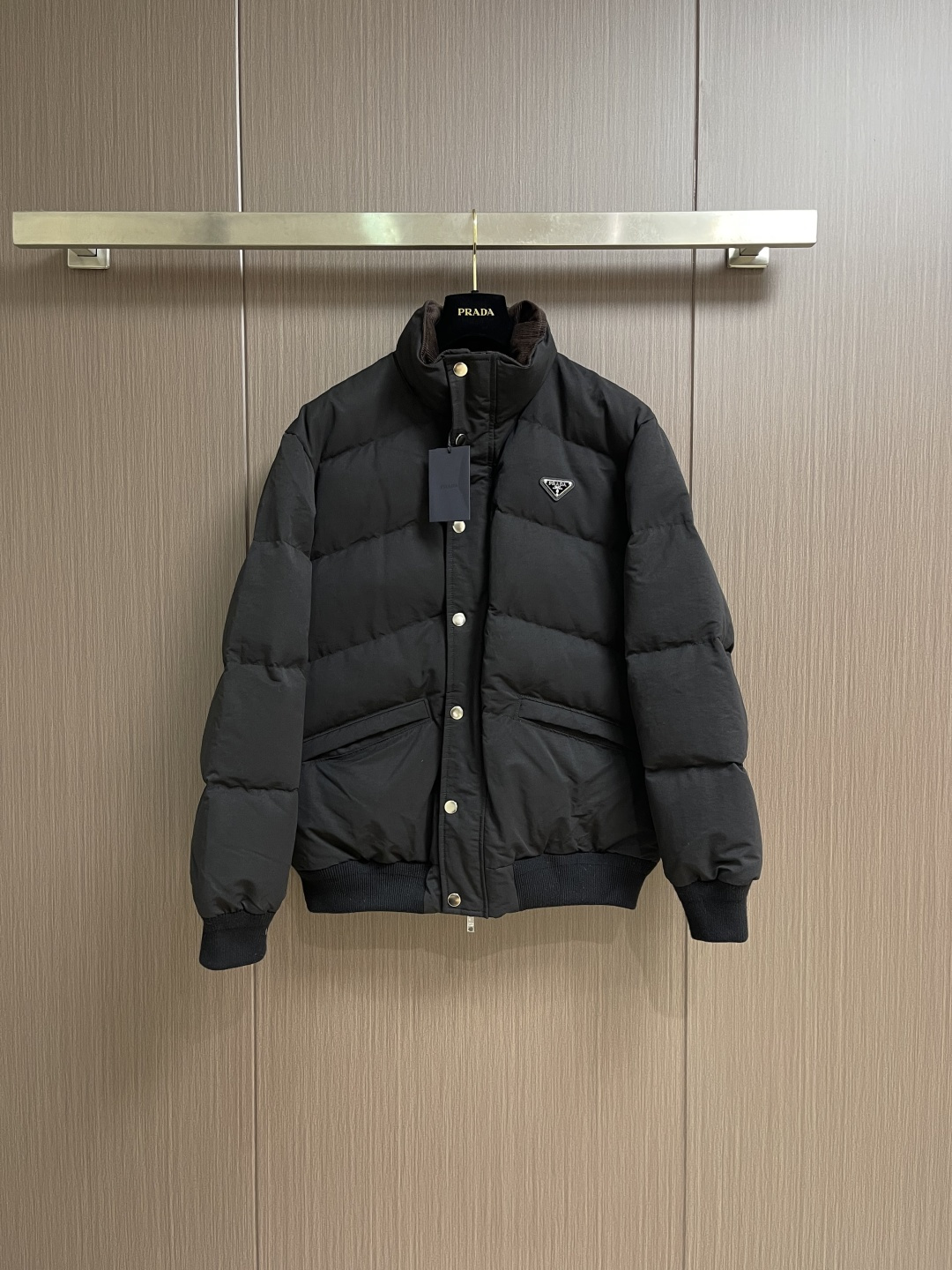 NO:597898,Prada  2025FW new autumn and winter down jacket. The stand-up collar is a luxurious winter hard currency. It is filled with 90% down. The down has high fluffiness and sufficient velvet content. It is lightweight but can lock in heat and get rid of the traditional bloat. It is made of high-count poplin fabric. The matte black tone has a cool and high-end feel. It is windproof and wear-resistant and has a crisp texture. It takes into account environmental protection concepts and practical performance. The classic triangle logo hardware decoration on the chest is used to suppress  The textured leather + metal rivet embellishment is a low-key but eye-catching identity mark; the zippers and snap buttons are engraved with the brand logo, the all-black color scheme is integrated with the fabric, and the texture is hidden in every opening and closing; the stand-up collar + ribbed edge design adapts to different body shapes while locking in warmth. The loose cut can be layered and is a 'universal' for autumn and winter commuting. Sizes 46-52, prada, jackets  & coats,down jacket,alexander wang19860909Prada 2025FW秋冬新品羽绒服外套,立领机能奢感的冬日硬通货,内里填充90绒,绒朵蓬松度高、绒子含量足,轻量却能锁住热量,摆脱传统的臃肿厚重；采用高支府绸面料,哑光黑调自带冷冽高级感,防风耐磨且质感挺括,兼顾环保理念与实用性能.胸前经典三角标五金装饰,以压纹皮革＋金属铆钉点缀,是低调却醒目的身份标识；拉链、按扣均刻印品牌标识字样,全黑配色与面料融为一体,质感藏在每一处开合；立领＋罗纹收边设计,适配不同身形的同时锁住暖意,宽松剪裁可叠穿、,是秋冬通勤的「万能」.尺码46-52,,prada,jackets & coats,down jacket,alexander wang,Men's clothing