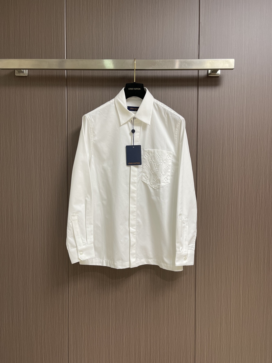 NO:596882,LV  Embossed pocket lapel long-sleeved shirt, twill woven fabric, standard version of peak lapel, hidden front placket, pearlescent buttons at the top, equipped with base, chest pocket with logo embossing, obvious twill texture on the front of the fabric, blurred on the back. Single yarn is used in both the warp and weft directions, the thread density is similar, the warp density of the fabric is slightly higher than the weft density, and the hand feel is relatively soft  Soft. The fabric has excellent stability, is not easy to deform, and prevents bulging; cotton fiber has good hygroscopicity, which keeps the fabric in a water balance state, making people feel comfortable and adding to the sophistication of the fabric. The concave and convex embossing process is heated and shaped by the upper and lower dies, and the rollers press the fabric at a certain temperature, and the production is completed through mechanical embossing.  Produce three-dimensional hierarchical convex surface. The fabric produces a concave and convex pattern with a relief-style three-dimensional effect and a special gloss effect. The three-dimensional shape, pattern and text have a strong three-dimensional effect, adding a decorative art effect, with clear layers, concentrated three-dimensional image, and accurate perspective angle. The collar can be adjusted with buttons for tightness.  Formal feeling and comfort; rear pleats and tabs are classic shirting techniques. The pleats provide additional room for movement, and the ribbons can maintain the shape of the shirt when hanging. The button front adopts custom buttons with matching positioning. These details together ensure the practical function and crisp shape of the shirt. Sizes XS-L, Louis  vuitton,shirts,alexander wang19860909LV 压花口袋翻领长袖衬衫,斜纹梭织面料、翻尖领标准版型、隐藏式前襟、顶端珠光纽扣、配有底座、胸袋呈现标识压纹、织物正面斜纹纹路明显,反面比较模糊.经纬向均用单纱,线密度接近,织物经密略高于纬密,手感比较柔软.面料具有极好的稳定性,不易变形、防鼓包；棉纤维具有较好的吸湿性,使织物保持水平衡状态,使人感觉舒适,增添了面料的精致度.凹凸压花工艺由上下模加热定型,轧辊在一定温度下压轧织物,通过机械压印来完成产生立体层次凸面.织物产生具有浮雕风格的立体效应和特别的光泽效果的凹凸花纹的工艺,制作立体造型图案文字有较强的立体感,增添装饰艺术效果,层次清晰、立体形象浓缩、透视角度准确.衣领可通过纽扣调节松紧,兼顾正式感与舒适度；后部褶裥与袢带是经典衬衫工艺,褶裥提供额外的活动余量,祥带则可在悬挂时保持衬衫形态.纽扣前襟选用定位相符的定制纽扣,这些细节共同确保了衬衫的实用功能与挺括造型.尺码XS-L,,louis vuitton,shirts,alexander wang,Men's clothing