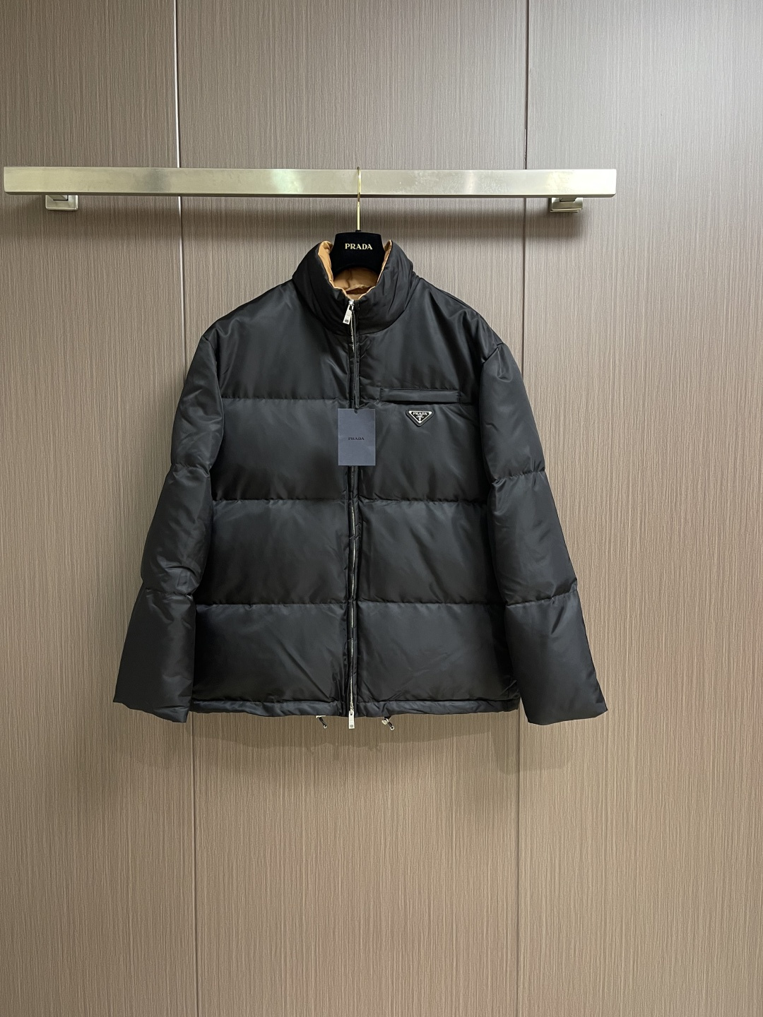 NO:600216,Prada The nylon color-blocked stand-collar down jacket is made of regenerated nylon fabric made of nylon. It is woven into a tight and tough fabric through advanced textile technology. It improves the strength of the frame and effectively blocks the invasion of cold wind and locks in the warm air generated by the down layer. After tight weaving and special processing, it is waterproof and windproof. The surface forms a certain lotus leaf effect, is wrinkle-resistant and not easy to deform, and is easy to take care of daily. The inner lining is made of polyamide woven polyamide. The sugar brown nylon fabric forms a strong color contrast when folded, just like the molten gold of the setting sun is injected into the deep night sky. The polyamide fiber is famous for its extremely high strength and excellent skin-friendly feeling. It feels silky and smooth, which avoids the risk of being worn when wearing heavy clothes. It can cause friction and discomfort. It works together with the outer layer of nylon to build a breathable, temperature-locking, and extremely comfortable microclimate environment, allowing warmth and care to be online at all times without feeling stuffy or restrictive. It uses 90 white duck down. The fill power reaches 220g, ensuring excellent thermal insulation performance. After strict screening and processing, the velvet is not easy to velvet. It is cut with a 6 cm high stand-up collar, which fits the neck line without being oppressive. It is as warm as a 'second skin' in the cold wind. Warm. The junction between the collar and the zipper adopts a bevel splicing process to avoid the stiffness of the traditional stand-up collar and make it more flexible when turning the head. There are built-in metal adjustment buckles on both sides of the hem. Pull it down gently to tighten the waistline, and lift it up to restore the loose silhouette - through The metal surface of the adjustment buckle is treated with PVD coating, which is wear-resistant and corrosion-resistant, and will last a long time. A quilting machine is used to divide the fabric into 8 independent velvet grids, and the stitch length is strictly controlled at 3 stitches cm. The stitch error does not exceed 0.1mm. The sutures are made of high-strength nylon threads. The tensile force test reaches 20N (approximately 2kg load-bearing), which eliminates the risk of suture breakage. Sizes S-XL, prada, jackets & coats,down jacket,alexander wang19860909Prada 尼龙拼色立领外套羽绒服,选用锦纶制成的再生尼龙面料,通过先进的纺织技术,编织成紧密且坚韧的布料,提升骨架强度有效阻挡冷风侵袭,锁住羽绒层产生的暖空气,经过紧密的编织工艺和特殊处理之后使其具备防水防风等功能,表面形成一定的荷叶效应,同时抗皱不易变形,易于日常打理.内衬采用了聚酰胺编织而成的焦糖棕色尼龙面料,翻折时形成强烈色彩对冲,宛如将落日熔金注入深邃夜空.聚酰胺纤维以其极高的强度与卓越的亲肤感著称,触感如丝般顺滑,避免了穿着厚重时可能产生的摩擦不适.它与外层尼龙协同工作,共同构建了一个透气、锁温、且极度舒适的微气候环境,让温暖呵护时刻在线,却毫无闷热与束缚感,选用90白鸭绒,蓬松度达220g,确保保暖性能卓越.绒子经过严格筛选与处理之后,不易钻绒.6公分加高立领剪裁,贴合颈部线条却不压迫,,寒风中宛如'第二层肌肤'般温暖.领口与拉链衔接处采用斜角拼接工艺,避免传统立领的呆板感,转头时更显灵动.下摆内置双侧金属调节扣,轻轻下拉即可收紧腰线,上提则恢复宽松廓形﹣﹣通勤时利落修身,户外时自由无拘.调节扣金属表面经PVD镀层处理,耐磨抗腐蚀,历久弥新.采用绗缝机,将面料分割为8个独立绒格,针距严格控制在3针cm,线迹误差不超过0.1mm,缝线选用高强度尼龙线,拉力测试达20N（约2kg承重）,杜绝因缝线断裂导致的.尺码S-XL,,prada,jackets & coats,down jacket,alexander wang,Men's clothing