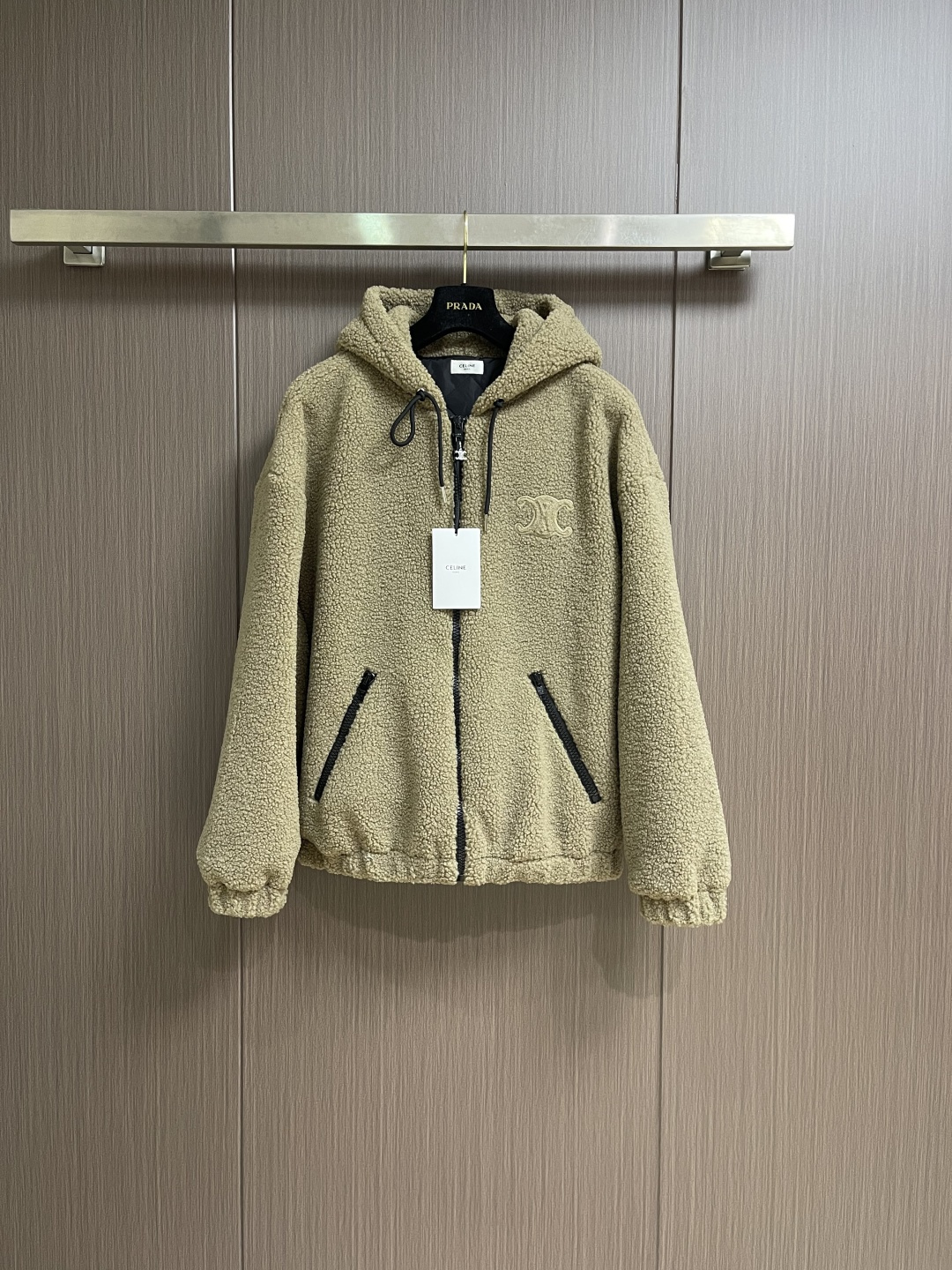 NO:600214,Celine  The suede hooded jacket decorated with the brand logo is made of polyester filament and is knitted through a circular knitting machine. The warp and weft yarns are woven into each other into a double-sided knitted structure. The front and back are flat coils. The fabric is formed after a series of processes such as dyeing, raising, carding, shearing, and polarization. The suede texture is soft.  The fiber characteristics make it almost non-absorbent, and can quickly drain sweat to the outer layer of the fabric and evaporate quickly, maintaining good breathability. The suede surface can lock the air and form a stagnant air layer around the body, effectively preventing heat loss and providing good thermal insulation performance. The inner quilting adopts a quilted cannage pattern, which is precisely adjusted by the seamstress.  The speed and stitch density of the machine make the stitches smooth and even during operation. After completion, regular diagonal quilting lines are formed, which inadvertently improves the overall texture when putting on and taking off. The embroidery patch tightly fixes the fabric and padding material to the frame of the embroidery machine, and the embroidery machine uses sparser stitches along the pattern of the padding layer.  Outline the filling area of the pattern, then run the pattern of the overlay, and use dense stitches to perfectly cover the foam padding layer to form a slightly raised Arc de Triomphe shape. After the final finishing, the edges of the patch are burr-free and the pattern is clear. Sizes S-XL, celine, jackets  & coats,hats,alexander wang19860909Celine 饰品牌标识仔章绒面连帽外套,面料选择涤纶长丝通过针织圆机,将经纱和纬纱相互圈套编织成双面针织结构,正面和背面都是平整的线圈.再通过染色、起毛、梳毛、剪毛、摇粒等一系列流程之后形成的面料.绒面质地柔软,纤维特性使其几乎不吸水,能将汗迅速排到面料外层并快速蒸发,保持良好的透气性.绒面能锁住空气,再身体周围形成一层不流动的空气层,有效防止热量流失,起到良好的保暖性能.内里绗缝采用绗缝藤格纹,缝纫师精确调整机器的速度和针脚密度,作业中线迹平滑、均匀.完成之后形成具有规则的斜向绗缝线条,穿脱时不经意间提升整体质感.绣花贴饰将面料和垫衬材料一同紧绷地固定在绣花机框架上,绣花机沿着垫衬层的版迹运用较稀疏的针迹勾勒出图案的填充区域,紧接着运行覆盖层的版迹,用密集的针迹完美地覆盖在泡沫垫衬层之上,从而形成微凸起的凯旋门形状.最后通过整理之后,贴饰边缘无毛刺,图案清晰.尺码S-XL,,celine,jackets & coats,hats,alexander wang,Men's clothing