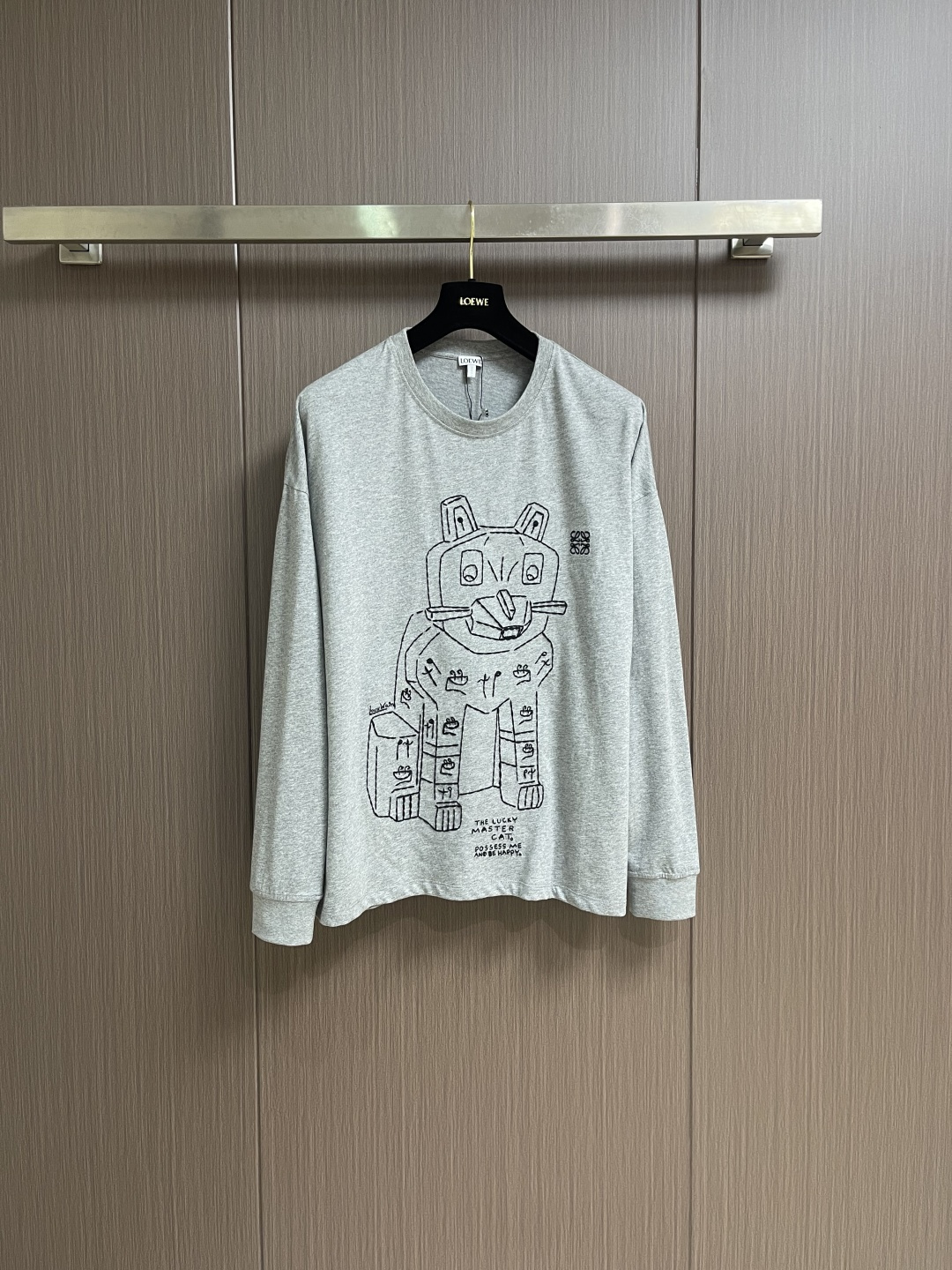 NO:645109,Loewe Stone Cat round neck long-sleeved T-shirt, the main body is made of 24S special compact cotton to make plain knitted fabric, with a weight of 180g. The high-count combed cotton yarn eliminates most of the short hairiness through the compact spinning process, making the yarn smoother and stronger. The woven fabric structure is extremely dense, flat and soft, with excellent anti-pilling ability and durability, while retaining the natural advantages of pure cotton, breathable and skin-friendly. The neckline is made of 32S 1x1 ribbing  Weighing 300g, the finer yarn count creates a more delicate and tight thread, which provides better elasticity and deformation resistance than ordinary ribs, ensuring that the neckline can still remain crisp after being put on and taken off many times. The rice grain line embroidery process uses special ultra-fine embroidery thread and high-density stitching to create a pattern outline as delicate and continuous as grains. Its core feature is the precise arrangement of ultra-fine stitches.  , it takes 12-15 stitches per centimeter to form full lines, and the edges present a micro-waving effect with a hand-made feel. A stroke-like thickness gradient and flow are achieved on the fabric. The overall pattern is light, breathable and smooth to the touch. It looks like a line outline from a distance, but the texture of interwoven fibers can be seen up close. It is especially suitable for expressing delicate details such as logo outlines and geometric borders. Anagram  The embroidery adopts three-dimensional embroidery technology, and the logo clearly restores the spacing curve. It is carried out with glossy mercerized embroidery thread, combined with complex embroidery needlework and fine detail processing, creating a three-dimensional relief embroidery effect. The classic trademark letter design, fine stitching and dense embroidery, clear fonts and strong lines and three-dimensionality. The overall line is straight and delicate, the fabric is comfortable and soft, the color is consistent and no color difference. It can be matched with the same style to create a fashionable look and control various occasions. Customized accessories, complete three labels, the same style for men and women!  Size XS-L,,loewe,tees,t-shirt,alexander wang19860909Loewe 石像猫圆领长袖T恤,主体采用24S特纺紧密棉打造平纹针织面料,克重180g.高支数的精梳棉纱通过紧密纺工艺消除了大部分短毛羽,使得纱线更光滑、强韧.织成的面料结构异常密实、平整且柔软,具有出色的抗起球能力和耐用性,同时保留了纯棉透气亲肤的天然优势.领口则选用32S 1x1罗纹 克重300g,更细的纱支编织出更细腻紧密的螺纹,提供了优于普通罗纹的回弹性与抗变形能力,确保领口历经多次穿脱后仍能保持挺括,米粒线条刺绣工艺通过特制极细绣线与高密度针法,塑造出如谷物般细腻连续的图案轮廓.其核心特点在于超细线迹精密排列,每厘米需达12-15针方能形成饱满线条,边缘呈现手工感的微波动效果.在面料上实现笔触般的粗细渐变与流动感,图案整体轻盈透气且触感平整,远观似线条勾勒,近看可见纤维交织的肌理,尤其适合表现徽标轮廓、几何边框等精致细节处理.Anagram 刺绣采用立体刺绣工艺,徽标清晰还原间距曲线.精选具有光泽感的丝光绣线进行,机结合复杂刺绣针艺,精细的细节处理,造就了立体浮雕的刺绣效果.经典商标字母设计,刺绣精细针法绵密,字体清晰且线条感和立体感强.整体走线平直细腻,面料舒适柔软,颜色一致无色差 能与同款搭配营造时尚造型,驾驭各种场合,定制辅料,三标齐全,男女同款！尺码XS-L,,loewe,tees，t-shirt,alexander wang,Men's clothing