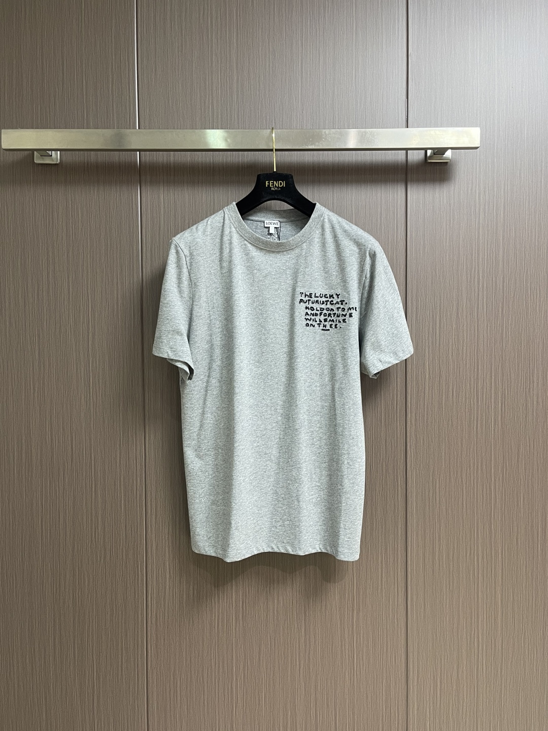 NO:645111,LOEWE  White cat floral gray round neck short-sleeved T-shirt, cotton jersey fabric. The main body is made of 24S special compact cotton to create a jersey fabric with a weight of 180g. The high-count combed cotton yarn eliminates most of the short hairiness through the compact spinning process, making the yarn smoother and stronger. The woven fabric structure is extremely dense, flat and soft, with excellent anti-pilling ability and durability, while retaining the natural advantages of pure cotton, breathable and skin-friendly. The neckline is made of 32S  1x1 rib  The weight is 300g, and the finer yarn count creates a more delicate and tight thread, which provides better elasticity and anti-deformation than ordinary ribs, ensuring that the neckline can still remain crisp after being put on and taken off many times. Multiple embroideries are combined, and the embroidered letters on the chest are chain embroidered.  The stitching is three-dimensional and full, with a unique woven texture and a soft touch; the craftsmanship ensures that the outline of the letters is clear, strong and durable. Its function is to highlight the brand or design theme on the front in a simple and exquisite way, and form a contrast between the primary and secondary and the traditional and simple with the more complex patterns on the back.  Futurist  Cat cross-stitch is a computer embroidery process that simulates traditional hand-made cross-stitch. A pixelated pattern is formed through the precise arrangement of countless 'X'-shaped stitches. Its function is to create a unique retro feel, a hand-made feel and a rich texture effect, forming an interesting space-time dialogue with the futuristic theme, giving the pattern profound artistic value and unique visual impact. Anagram embroidery uses three-dimensional embroidery technology, and is filled with multiple layers of embroidery thread to make the logo clear, full and protruding from the surface of the fabric. Classic trademark letters  Design, embroidery is fine and dense, the fonts are clear and have a strong sense of lines and three-dimensionality. Simple vertical round neck short-sleeved version, the pattern is developed to be extremely straight cut, the knitted material has certain stretchability, and the upper body will not be tight. The round neck is stitched with ribs of the same color at the neckline, and the back  The inner striping process of the collar effectively prevents the neckline from deforming after repeated wear and washing. The fitted shoulder line, bottom hem and cuffs are trimmed with special machines and open stitching. Sizes XS-L, loewe, T-shirt, tees, t-shirt, alexander  wang19860909LOEWE 白猫花灰圆领短袖T恤,棉质平纹针织面料,主体采用24S特纺紧密棉打造平纹针织面料,克重180g.高支数的精梳棉纱通过紧密纺工艺消除了大部分短毛羽,使得纱线更光滑、强韧.织成的面料结构异常密实、平整且柔软,具有出色的抗起球能力和耐用性,同时保留了纯棉透气亲肤的天然优势.领口则选用32S 1x1罗纹 克重300g,更细的纱支编织出更细腻紧密的螺纹,提供了优于普通罗纹的回弹性与抗变形能力,确保领口历经多次穿脱后仍能保持挺括.多刺绣结合处理,胸前的刺绣字母采用链式绣工艺,链式绣的线迹立体、饱满,带有独特的编织纹理,触感较为柔软；工艺处理确保字母轮廓清晰、牢固耐用.其作用在于以简洁而精致的方式在正面点明品牌或设计主题,与背面更复杂的图案形成主次和繁简的对比. Futurist Cat十字绣这是一种模拟传统手工十字绣的电脑刺绣工艺.通过无数个'X'形针脚的精确排列,来构成像素化的图案.它的作用是创造出独特的复古感、手工感和丰富的肌理效果,与未来主义主题形成有趣的时空对话,赋予图案深厚的艺术价值和独特的视觉冲击力.Anagram刺绣采用立体刺绣工艺,通过多层绣线填充,使标识清晰、饱满且凸出于面料表面.经典商标字母设计,刺绣精细针法绵密,字体清晰且线条感和立体感强.简约垂直圆领短袖版型,对版纸样开发极简直身剪裁,针织材质具有一定延展性能,上身不会紧紧束身.圆领同色罗纹拼接领口,后领口内贴条工艺,有效防止多次穿洗后领口变形,合身肩线,底摆与袖口专机坎车明线收边.尺码XS-L,,loewe,T-shirt,tees，t-shirt,alexander wang,Men's clothing