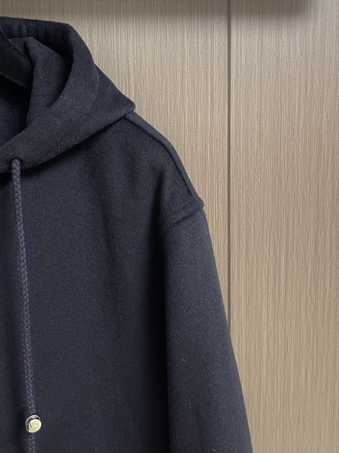 Loewe 皮标连帽长款大衣，以深邃的藏蓝为主色调，帽檐外侧中央镶嵌一枚哑光黑Logo皮标，优雅大气。人