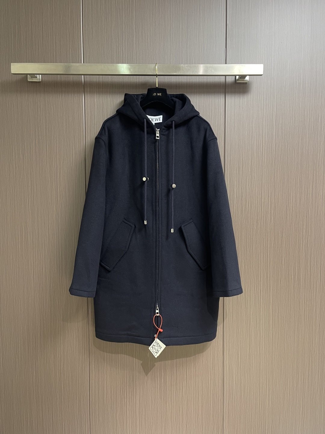Loewe 皮标连帽长款大衣，以深邃的藏蓝为主色调，帽檐外侧中央镶嵌一枚哑光黑Logo皮标，优雅大气。人