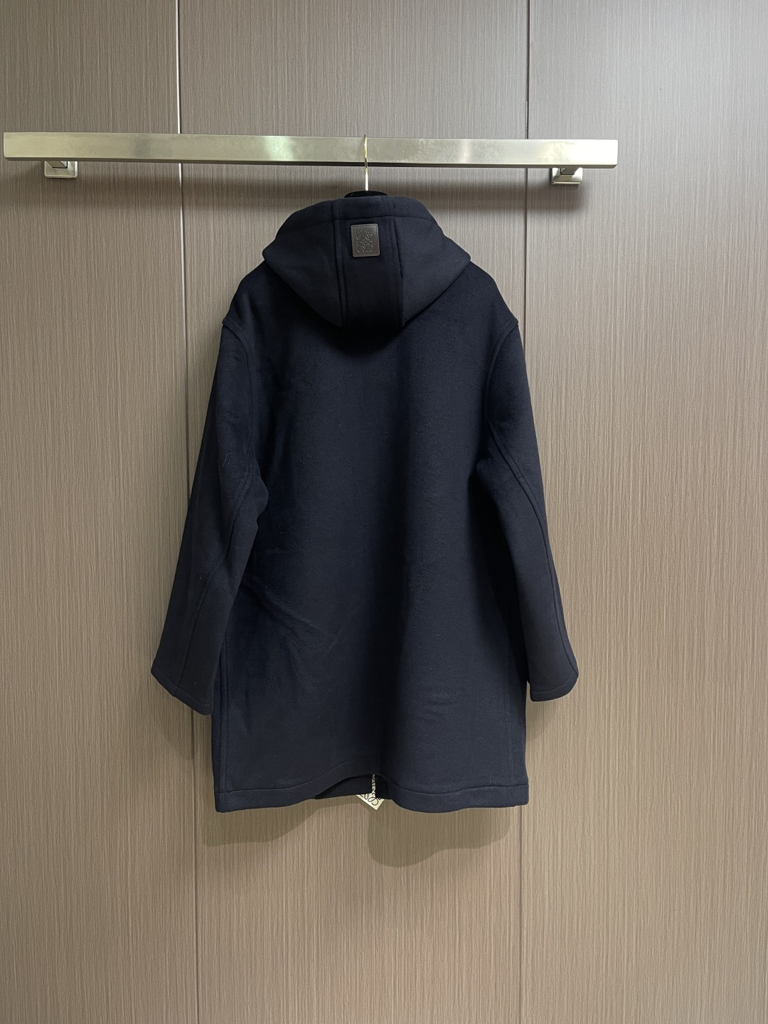 Loewe 皮标连帽长款大衣，以深邃的藏蓝为主色调，帽檐外侧中央镶嵌一枚哑光黑Logo皮标，优雅大气。人