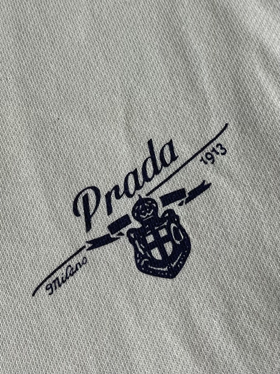 Prada 学院拉链连帽外套，采用32支单纱面＋16支纱底的卫衣面料结构，克重为320gm2；搭配的21