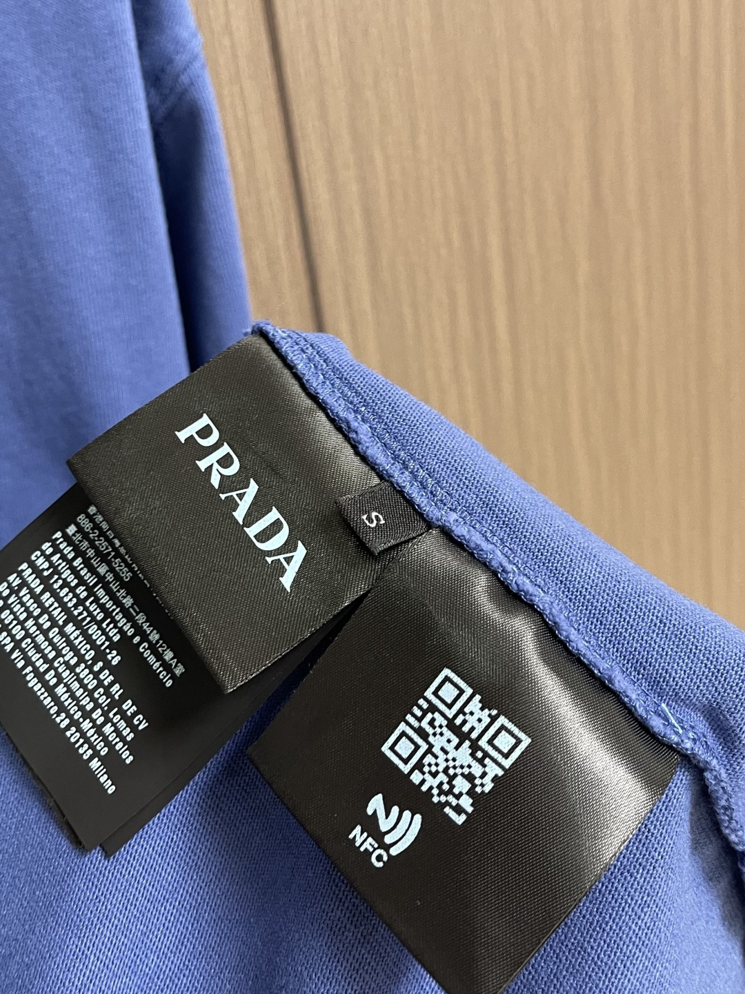 Prada 蓝三角圆领长袖T恤，采用12支精棉平纹针织面料，克重为230gm2；搭配32支双纱高罗纹，克