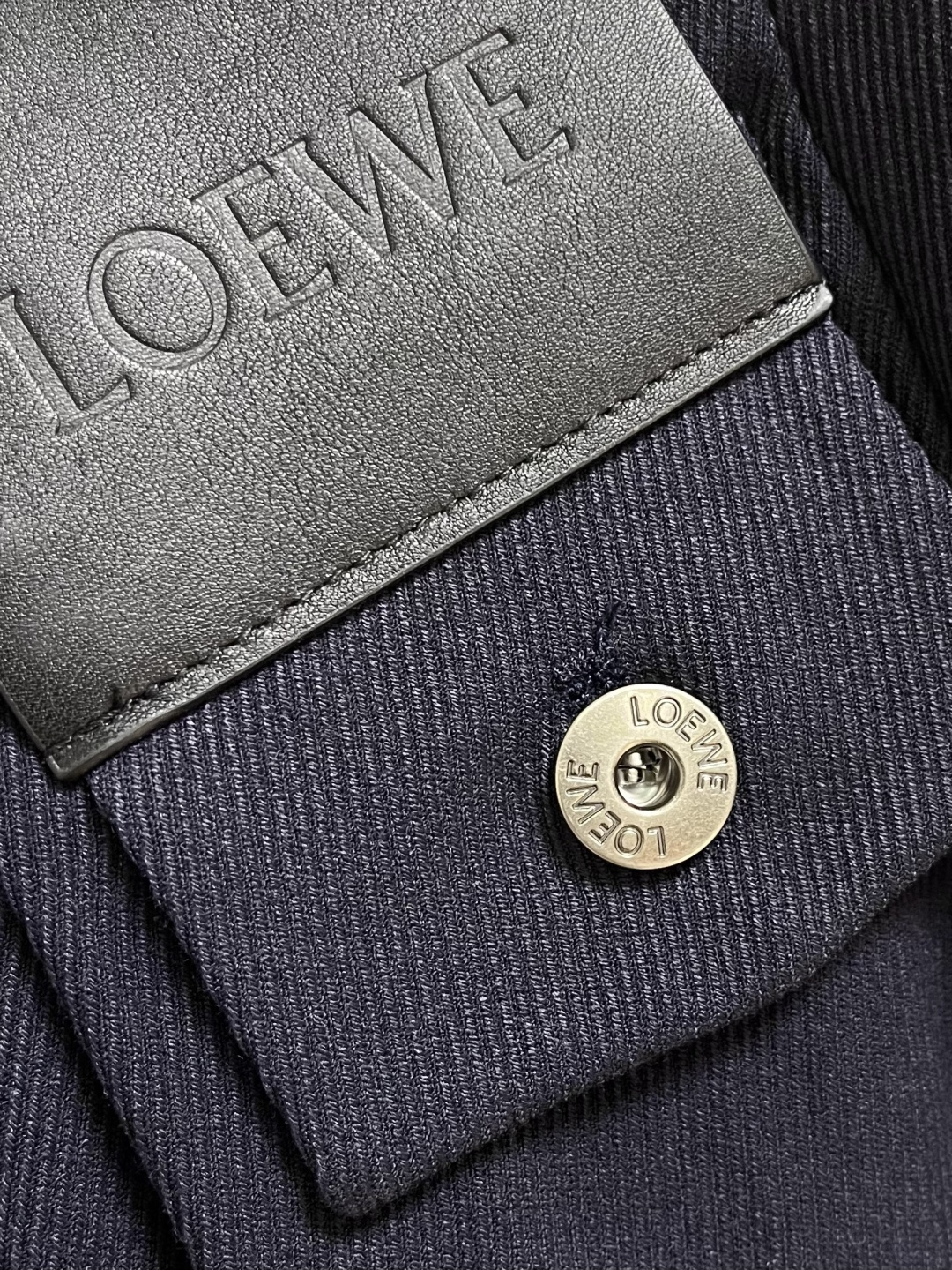 Loewe 皮牌休闲裤，定制丝光雾面羊毛，以雾感深海军蓝为主色调，腰头正面饰有LOE 压纹皮革贴片，与纽