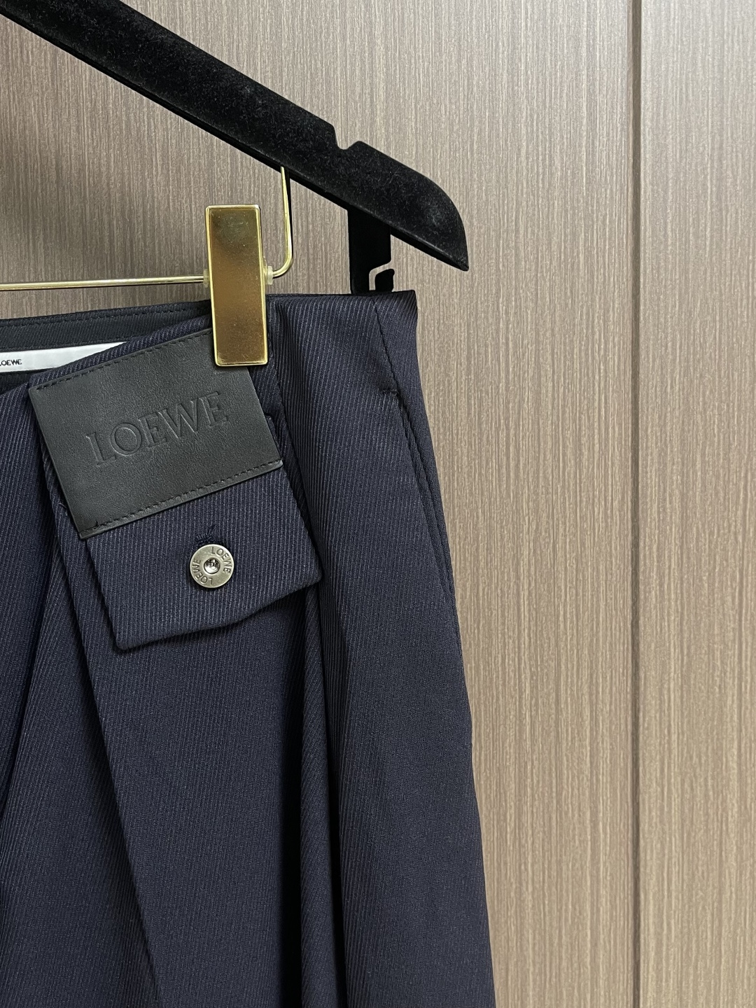 Loewe 皮牌休闲裤，定制丝光雾面羊毛，以雾感深海军蓝为主色调，腰头正面饰有LOE 压纹皮革贴片，与纽