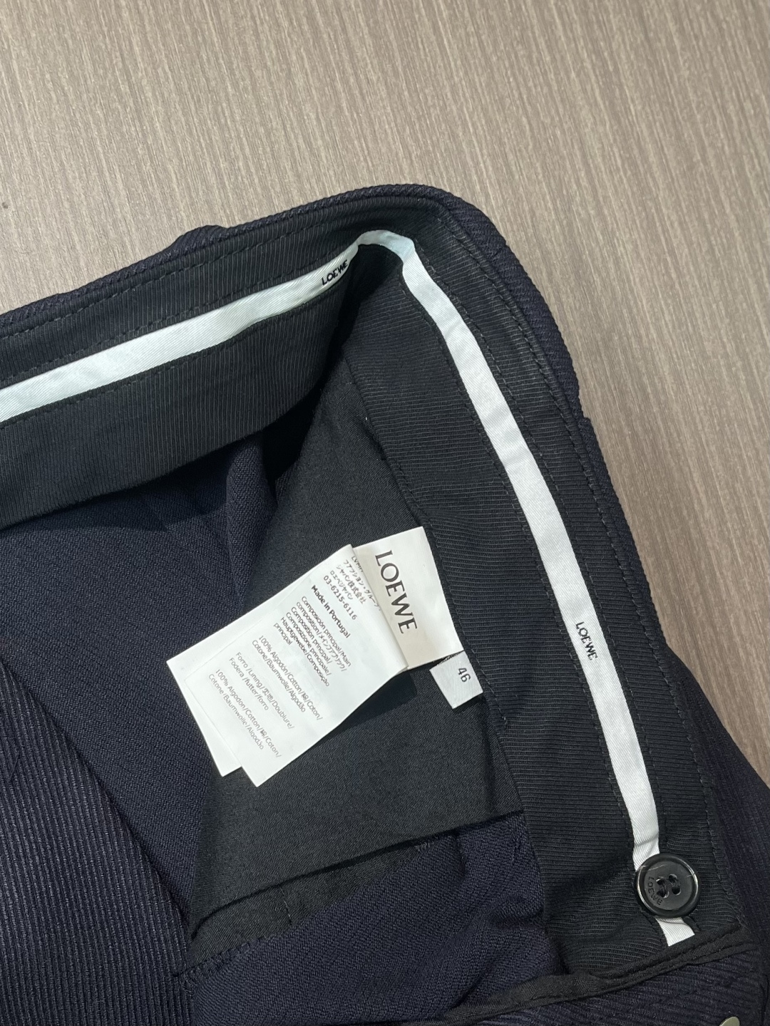 Loewe 皮牌休闲裤，定制丝光雾面羊毛，以雾感深海军蓝为主色调，腰头正面饰有LOE 压纹皮革贴片，与纽