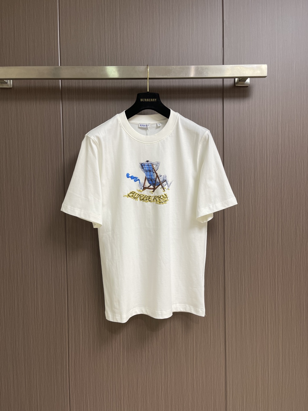 NO:831387,Burberry The beach lounger printed round neck short-sleeved T-shirt is made of 15-count special woven compact cotton jersey fabric with a weight of 230gm2; 32-count high-weight 1x1 rib with a weight of 340gm2. The 15-count yarn is thicker, the fabric has a strong texture and a crisp texture. In the finishing stage before printing, mercerization is a key process. The fabric significantly enhances the light gloss and smoothness; at the same time, mercerization can improve the uniformity of dye adsorption and make the fabric background color fuller and more uniform. The neckline uses 32 high-weight 1x1 ribs. The woven structure makes the rib tissue denser and has excellent elastic recovery rate, which can effectively prevent the neckline from loosening and deforming after repeated wearing and taking off. The hand-painted artistic pattern uses dot paste printing + suede foam printing The combination of flower craftsmanship achieves a layered visual effect. First, dot paste printing uses a fine screen to overprint the color paste in the form of dots to form a gradient, breathable and translucent effect, which is used to express the texture and light and shadow levels of the plaid lounge chair. Suede foam printing prints foamed slurry on specific areas of the pattern, and the foamed microspheres in the slurry expand when baked at high temperature , forming a three-dimensional raised and soft-touch suede texture. The combination of the two processes not only ensures the clarity and color saturation of the pattern details, but also vividly reproduces the lazy atmosphere of the leisurely scene through the concave and convex touch of the foam printing, forming a rigid and soft contrast with the stiffness of the medium-thick fabric. The overall wiring is straight and delicate, the fabric is comfortable and soft, and the color is consistent without color difference. It can be matched with the same style to create a fashionable look, and can be used in various occasions. Customized accessories, complete with three standards, same style for men and women! Size S-XL S size Bust 104 Shoulder width 45 Clothing length 70 Medium Bust 108 Shoulder width 46.5 Clothing length 72 L size Bust 112 Shoulder width 48 Clothing length 7419860909Burberry 沙滩躺椅印花圆领短袖T恤,采用15支特纺紧密棉平纹针织面料,克重为230gm2;32支高克重1x1罗纹,克重为340gm2.15支纱线较粗,织物肌理感强,质地挺括.在印花前的整理阶段,丝光处理是关键工序.面料显著增强光泽度与平滑感；同时,丝光能提升染料吸附均匀性,使面料底色更加饱满匀净.领口采用32支高克重1x1罗纹,编织结构使罗纹组织更加致密,弹性恢复率优异,能有效防止领口在反复穿脱后松垮变形.手绘艺术图案采用网点浆印花＋绒面发泡印花工艺结合,实现层次丰富的视觉效果.首先,网点浆印花通过细密网版将色浆以网点形式叠印,形成渐变、透气的半透明效果,用于表现格纹躺椅的纹理与光影层次.绒面发泡印花将发泡浆料印于图案特定区域,经高温烘烤时浆料中的发泡微球膨胀,形成立体隆起、触感柔软的绒面质感.两种工艺结合,既保证了图案细节的清晰度与色彩饱和度,又通过发泡印花的凹凸触感,生动再现了悠闲景致的慵懒氛围,与中厚面料的挺括形成刚柔对比.整体走线平直细腻,面料舒适柔软,颜色一致无色差 能与同款搭配营造时尚造型,驾驭各种场合,定制辅料,三标齐全,男女同款！尺码S-XL S码 胸围104 肩宽45 衣长70 M码 胸围108 肩宽46.5 衣长72 L码 胸围112 肩宽48 衣长74 XL码 胸围116 肩宽49.5衣长76,,burberry,T-shirt,tees，t-shirt,,Men's clothing