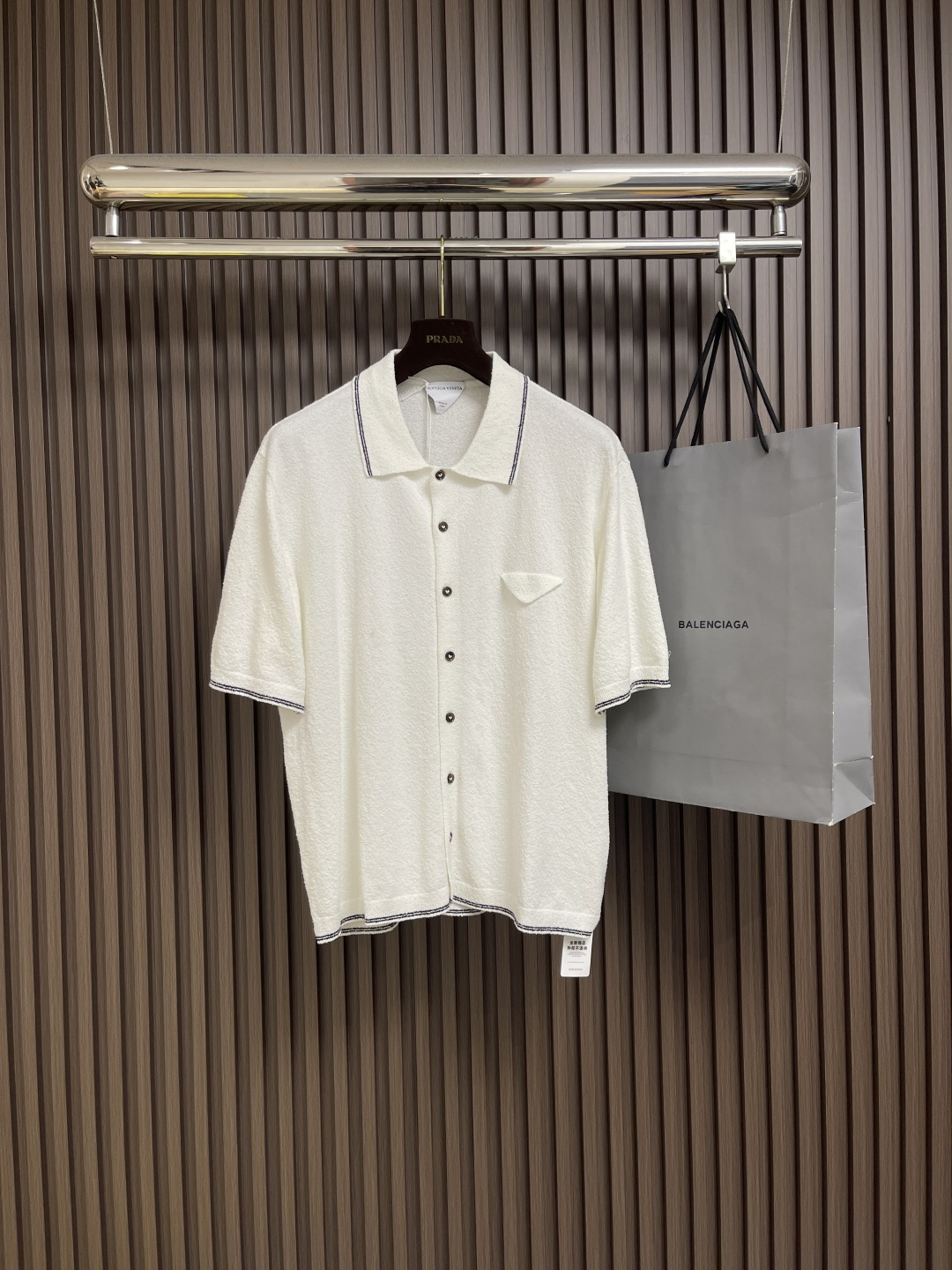 NO:461284,Bottega Veneta BV spliced ​​trim ring velvet short-sleeved shirt is made of high-quality pure cotton fabric, which feels soft and comfortable, with good breathability and drape. The shirt is mainly tone with pure white, and the neckline is classic lapel design and matched with buttons in the same color. The overall shape is simple and atmospheric. The designer carefully added color patch details to the cuffs and neckline, adding a low-key and fashionable feeling to the whole. The exquisite sewing process is reflected in the flat seam stitches, uniform stitch pitches and firm button fixings in each detail. The shirt style has been carefully cut, which not only maintains a loose and comfortable wearing experience, but also has a neat and capable outline. The fabric has been specially treated and has wrinkle resistance, which is convenient for daily care. Whether worn alone or as an inner wear, it can show an elegant and casual Italian style. Size S-M-L, bottega Veneta, bottega  veneta,shirts,T-shirt,alexander wang19860909Bottega Veneta BV 拼接饰边圈绒短袖衬衫,采用优质纯棉面料制成,触感柔软舒适,具有良好的透气性和垂坠感.衬衫以纯净白色为主调,领口采用经典翻领设计,搭配同色系纽扣,整体造型简约大气.设计师在袖口和领口处精心加入了拼色饰边细节,为整体增添了低调的时尚感.精湛的缝制工艺体现在每一处细节平整的车缝线迹、均匀的针距以及牢固的纽扣固定.衬衫版型经过精心剪裁,既保持宽松舒适的穿着体验,又不失利落干练的轮廓.面料经过特殊处理,具有抗皱性能,便于日常打理.无论是单穿还是作为内搭,都能展现优雅随性的意式风格.尺码S-M-L,,bottega veneta,bottega veneta,shirts,T-shirt,alexander wang,Men's clothing