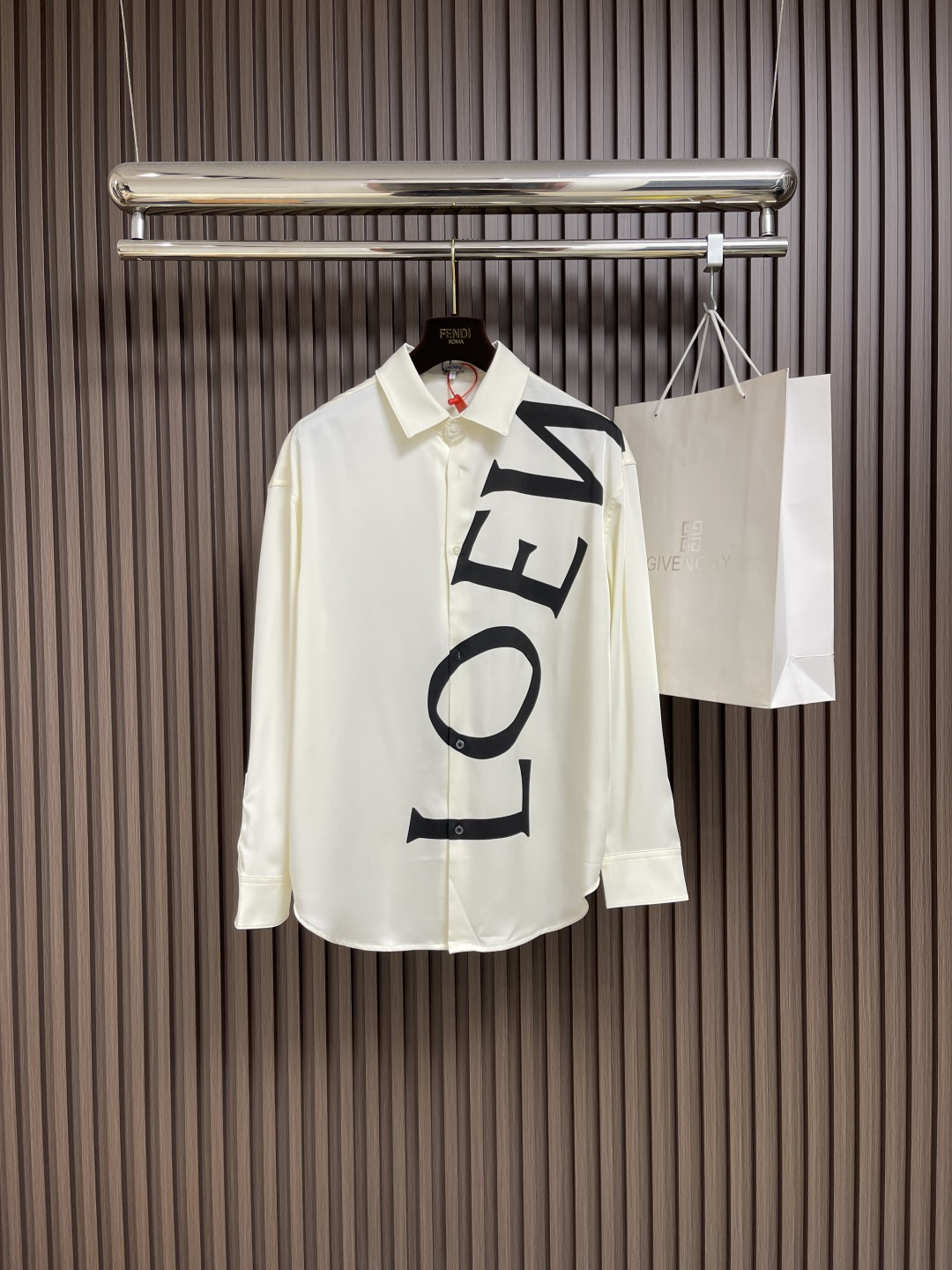 NO:498188,Loewe printed silk long-sleeved shirt, custom-made mulberry silk silk material, natural luster, with ivory white as the base color, and the ink-shadow black Loewe letters on it give a new visual focus in a very tense posture, and use a dynamic and irregular beauty to declare the brand's dignity. Imported slurry color printing is drawn, and printed on the dyed fabric with dyed agent, destroying the dye and forming a pattern printing process. When the dye is drawn and dyed, colored patterns are printed with clear lines and fine patterns.  Strong color fastness. Butterfly puffing combination technology, inspired by the beautiful form of butterflies, through precise puffing techniques, a flexible fold effect like butterfly wings is created on the clothing, making the clothing more fitting to the body. Cloth roller dyeing, through roller dyeing equipment, the dye penetrates evenly and deeply into the cloth fibers, achieving a dyeing effect with full color and high color fastness. Size S-XL 36-38-40-42,,loewe,shirts,alexander wang19860909Loewe 印花丝绸长袖衬衫,定制桑蚕丝丝绸料,光泽自然,以象牙白为底色,而斜印其上的墨影黑Loewe字母以一种极具张力的姿态赋予了全新的视觉焦点,用一种动态不规则的美感来宣告着品牌的尊贵.进口浆彩拔印花,用拔染剂印在已经染色的织物上,将染料破坏,形成花纹的印花工艺,在拔染的同时印上彩色图案,线条清晰 图案精细 色牢度强.蝶韵捏褶合体省道技术,以蝴蝶的优美形态为灵感,通过精准的捏褶手法,在服装上塑造出如蝶翼般灵动的褶皱效果,使服装更贴合身体.布匹滚筒染色,通过滚筒式染色设备,使染料均匀且深入地渗透到布匹纤维中,实现色彩饱满 色牢度高的染色效果.尺码S-XL 36-38-40-42,,loewe,shirts,alexander wang,Men's clothing