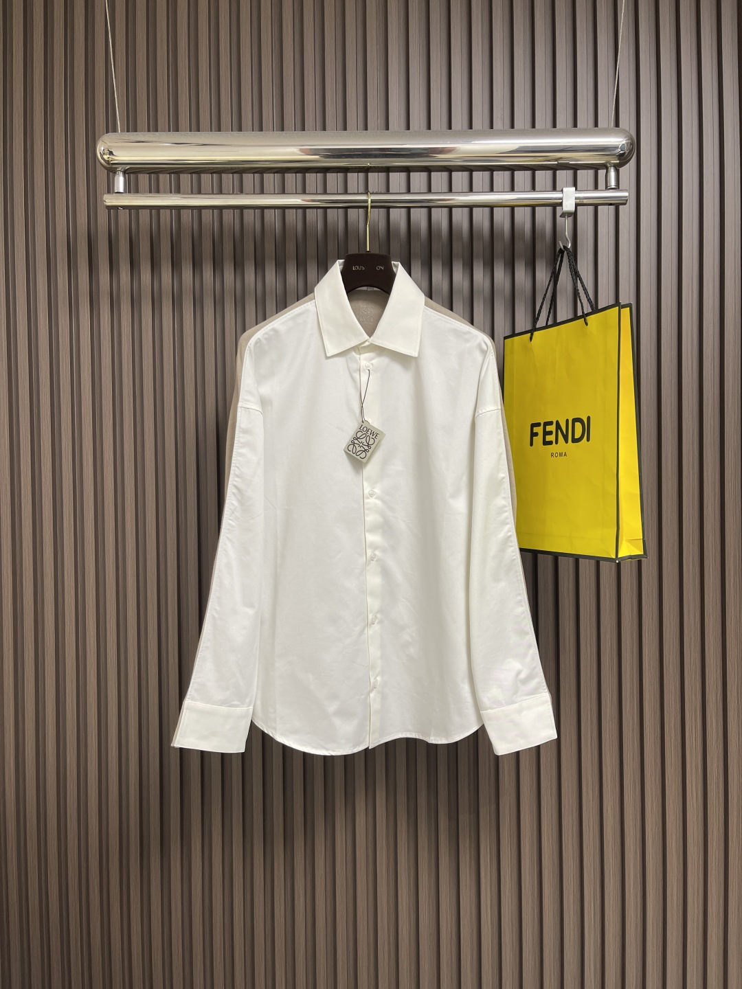 NO:540698,LOEWE  The front piece is made of high-strength cotton yarn and is made of a thin and extremely breathable fabric through a weaving process with high warp and low weft density. The surface is smooth and smooth, and the touch is as smooth as silk. At the same time, the cotton is natural skin-friendly and comfortable. Because the warp yarns are tightly arranged, the surface of the fabric has a longitudinal texture and soft luster, which enhances the visual sense of high-level. The back web is made of high-strength spinning technology and is woven into a moderately dense fabric with soft touch, which is soft and skin-friendly, and has a delicate velvet feel. The wool fiber has a natural hollow structure, which can lock in stationary air and form an excellent heat insulation layer. Even if it is light and thin, it has a good warmth effect. The head and needle are controlled by the high-precision calculation system of the embroidery machine under the back collar.  The joint operation of the rod and spool is carried out accurately in horizontal and vertical directions to form a stitch track, adjust the tension of the upper and lower lines to ensure that the stitch is flat and has no floating lines, forming an anagram embroidery with an error of ±0.1mm. The ironing master turns the collar straight, irons from the bottom to the upper end through high temperature and humid steam, applies pressure to smooth the wrinkles, and then turns to the front and repeat the operation. Turn to the collar and iron it into a curve, and press the collar to the bottom to maintain a firmness. The rotator cuff part uses the suspension method to avoid crushing the edges. After adjusting the fiber density through the ironing master's 'push, return, and pull' technology, it can better fit the human body curve. Size 36-38-40-42,,loewe,loewe,shirts,alexander  wang19860909LOEWE 罗意威拼接针织衬衫,前片选用高支棉纱通过经密高,纬密低的织造工艺制成轻薄且具有极佳透气性的面料.表面光滑平整,触感如丝绸般柔滑,同时保留棉的天然亲肤性,贴身舒适无异样感.因经纱紧密排列,织物表面呈现纵向纹理与柔和光泽,强化视觉高级感.后幅通过高支纺纱技术,用极细的羊毛纱线织成密度适中的面料,触感柔软亲肤,表面有细腻的绒感.羊毛纤维特性具有天然的中空结构,能锁住静止空气,形成绝佳的隔热层,即使轻薄,也有良好的保暖效果.后领下方处通过绣花机高精度的计算系统控制机头、针杆、线轴的协同作业,布料框架在水平和垂直方向精准移动,形成针迹轨迹,调整上线和下线张力,确保线迹平整无浮线,形成误差在±0.1mm的anagram刺绣.熨烫师将衣领翻立,通过高温湿蒸汽从底部向上端熨烫,施加压力抚平褶皱,再翻至正面重复操作.转至领口烫出弧形,后领压至最底以保持挺括.肩袖部分利用悬空法避免压死边缘.通过熨烫师的'推、归、拔'技术调整纤维密度之后,使更好的贴合人体曲线.尺码36-38-40-42,,loewe,loewe,shirts,alexander wang,Men's clothing