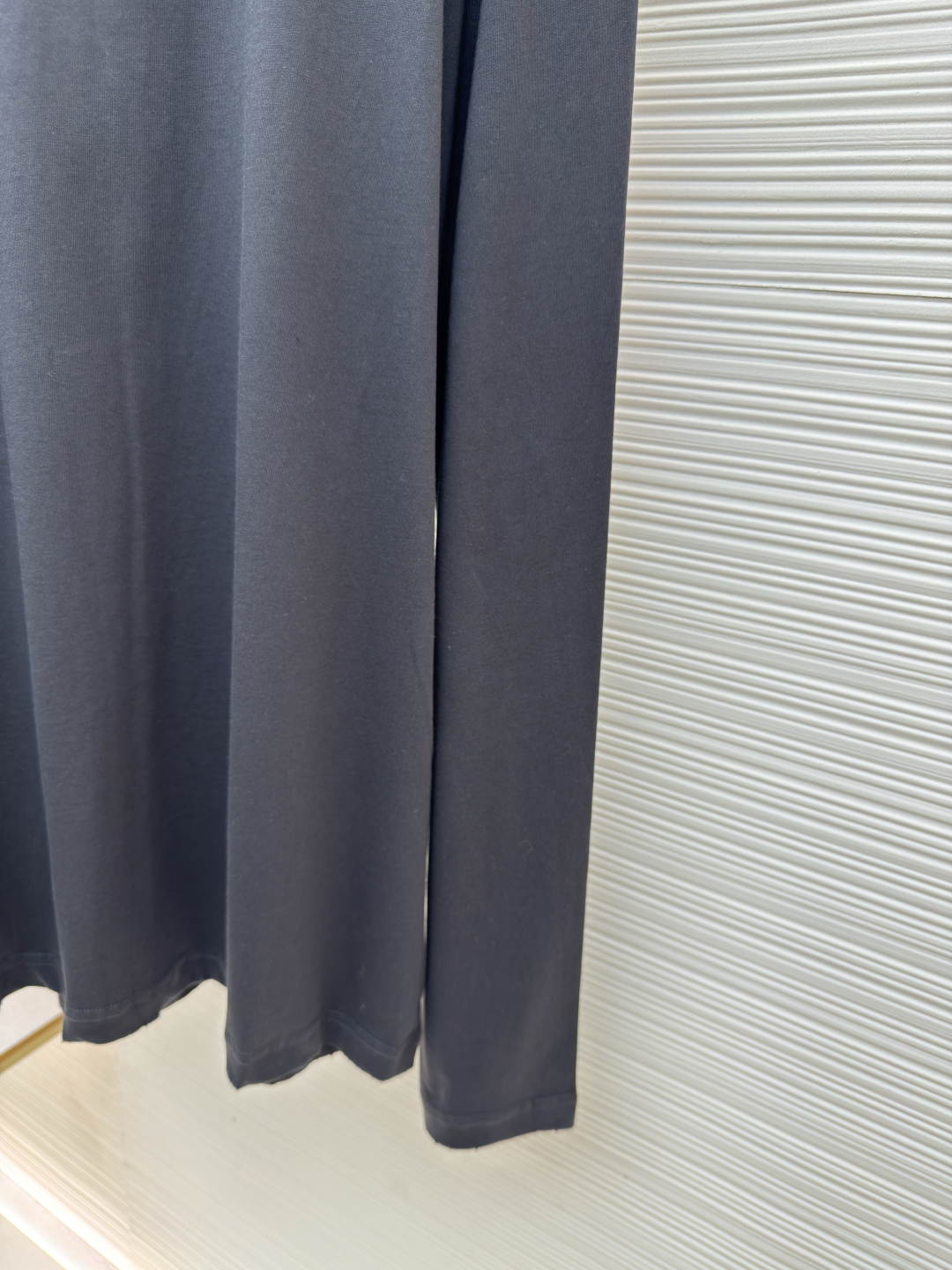 P125 Prada 铅笔灰长袖
●原版：8934购入开发
●货号:  1680720-A05
●面料：精梳平纹面料
●工艺：激光烧花制作
●版型：合身版型
●克重：约240克
●尺码：S-M-L-XL
●描述：定织50S 190G精梳平纹面料，非市场通用坯布，需从纱线配比、织机参数全程定制。通过精梳工艺去除短纤维杂质，确保纱线更长、更均匀，织物表面光洁无毛羽。  特殊定染铅笔灰色，单独调色而非使用标准色卡，需多次打样匹配Prada指定的低饱和度灰调。胸前三角激光烧花绣花定型：激光烧花：高精度激光雕刻，在面料表面碳化形成渐变蚀刻纹理，边缘需人工调试避免焦痕。  复合绣花：在烧花基础上叠加刺绣，线迹密度需与烧花图案对齐，防止面料变形。  立体定型：使用高温压烫或树脂涂层维持三角结构的浮雕感，避免洗后塌陷。整体走线平直细腻，面料舒适柔软，颜色一致无色差 能与同款搭配营造时尚造型，驾驭各种场合，定制辅料，三标齐全，男女同款！