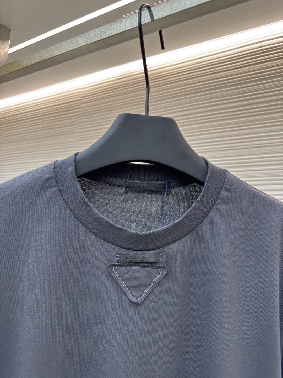 P125 Prada 铅笔灰长袖
●原版：8934购入开发
●货号:  1680720-A05
●面料：精梳平纹面料
●工艺：激光烧花制作
●版型：合身版型
●克重：约240克
●尺码：S-M-L-XL
●描述：定织50S 190G精梳平纹面料，非市场通用坯布，需从纱线配比、织机参数全程定制。通过精梳工艺去除短纤维杂质，确保纱线更长、更均匀，织物表面光洁无毛羽。  特殊定染铅笔灰色，单独调色而非使用标准色卡，需多次打样匹配Prada指定的低饱和度灰调。胸前三角激光烧花绣花定型：激光烧花：高精度激光雕刻，在面料表面碳化形成渐变蚀刻纹理，边缘需人工调试避免焦痕。  复合绣花：在烧花基础上叠加刺绣，线迹密度需与烧花图案对齐，防止面料变形。  立体定型：使用高温压烫或树脂涂层维持三角结构的浮雕感，避免洗后塌陷。整体走线平直细腻，面料舒适柔软，颜色一致无色差 能与同款搭配营造时尚造型，驾驭各种场合，定制辅料，三标齐全，男女同款！