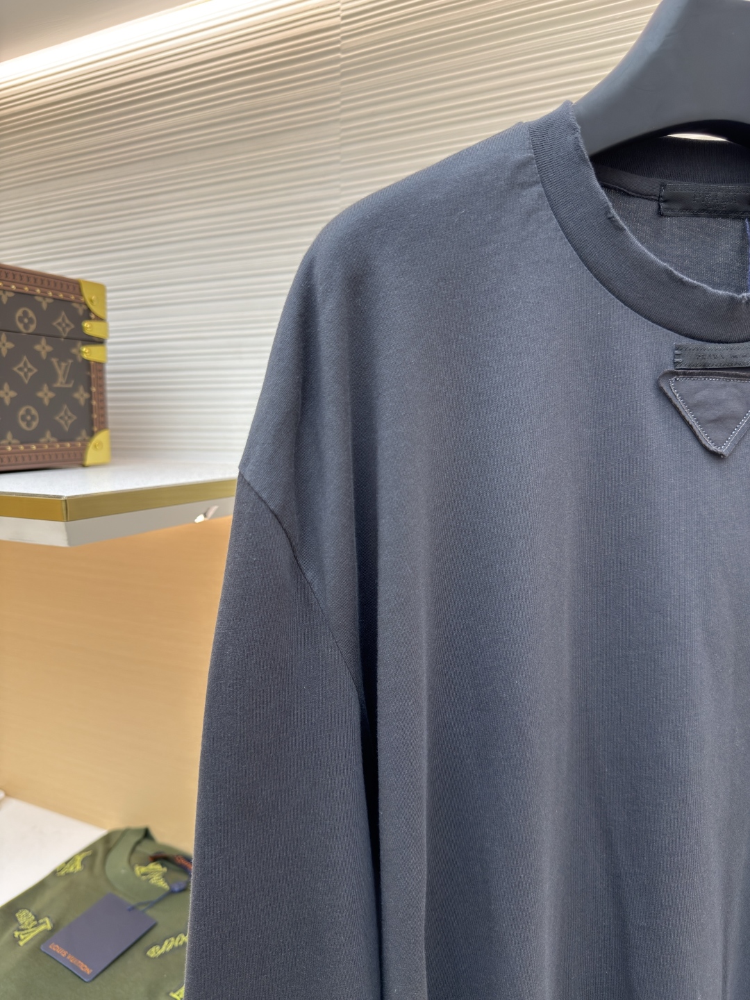 P125 Prada 铅笔灰长袖
●原版：8934购入开发
●货号:  1680720-A05
●面料：精梳平纹面料
●工艺：激光烧花制作
●版型：合身版型
●克重：约240克
●尺码：S-M-L-XL
●描述：定织50S 190G精梳平纹面料，非市场通用坯布，需从纱线配比、织机参数全程定制。通过精梳工艺去除短纤维杂质，确保纱线更长、更均匀，织物表面光洁无毛羽。  特殊定染铅笔灰色，单独调色而非使用标准色卡，需多次打样匹配Prada指定的低饱和度灰调。胸前三角激光烧花绣花定型：激光烧花：高精度激光雕刻，在面料表面碳化形成渐变蚀刻纹理，边缘需人工调试避免焦痕。  复合绣花：在烧花基础上叠加刺绣，线迹密度需与烧花图案对齐，防止面料变形。  立体定型：使用高温压烫或树脂涂层维持三角结构的浮雕感，避免洗后塌陷。整体走线平直细腻，面料舒适柔软，颜色一致无色差 能与同款搭配营造时尚造型，驾驭各种场合，定制辅料，三标齐全，男女同款！