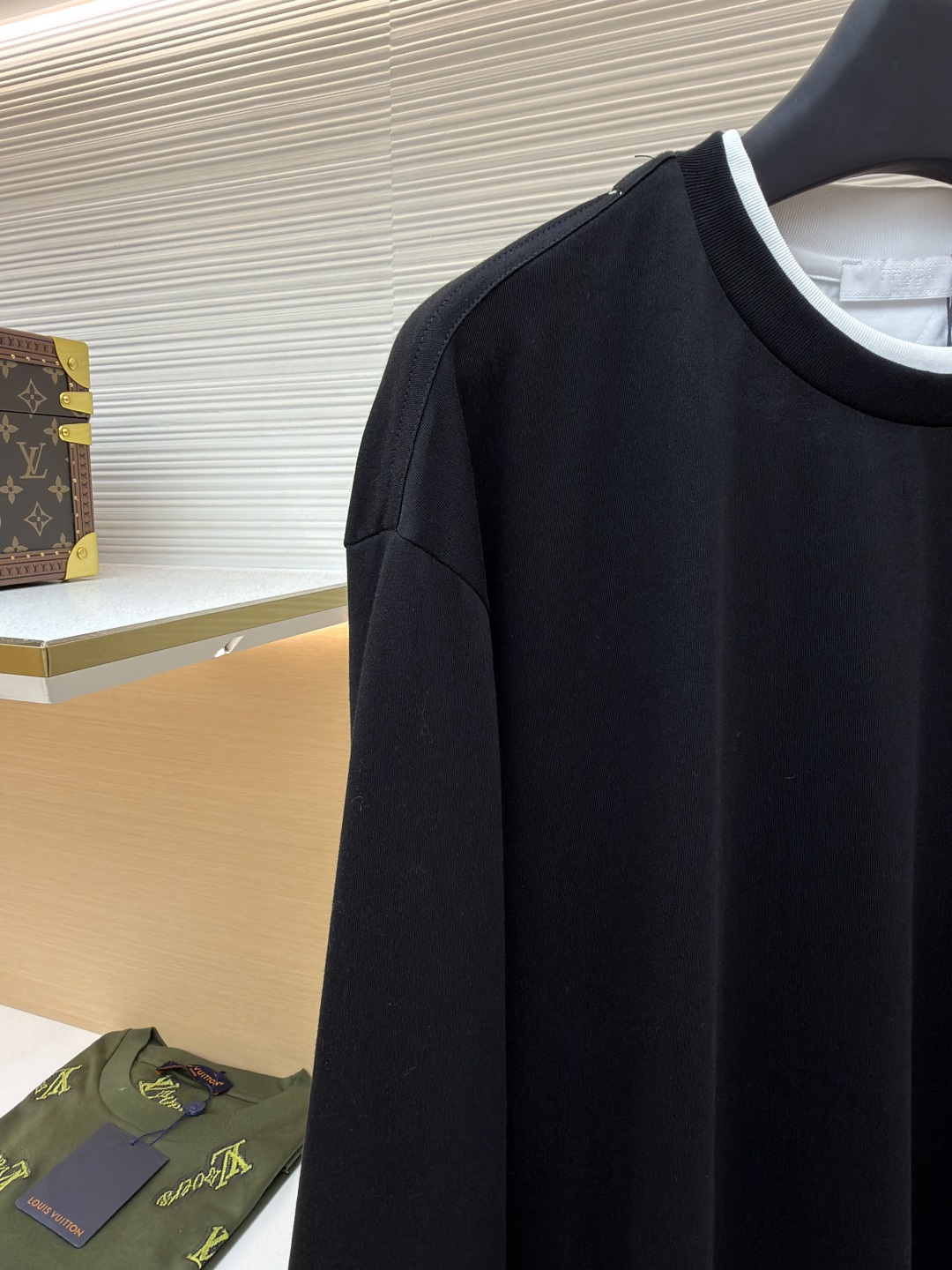 P140 Prada 三角标假两件长袖
●原版：6670购入开发
●货号：1680979-A20
●面料：精梳棉面料
●工艺：激光烧花制作
●版型：合身版型
●克重：约315克
●尺码：S-M-L
●描述：根据原版定制纱线，以达到特定的克重（200g/㎡）、厚度、韧性和手感。200克的重量确保了衣物具有良好的垂坠感和挺括度，不会轻飘也不会笨重。 “精梳” 工艺去除了棉纤维中的短绒和杂质，使得纱线更顺滑、强韧，织出的面料表面光洁、不易起球、触感细腻。“定染” 确保了颜色是专属且一致的，色彩饱和度与面料质感完美匹配，呈现出高级的单一色调。“假两件”设计是工艺智慧的体现。它并非简单地将两片布缝在一起，而是通过精密的一体化剪裁和拼接，模拟出两件衣物叠穿的层次效果。其复杂性在于无痕衔接：在领口、袖口和下摆处的拼接必须天衣无缝，模拟出内搭衣物的自然露出状态。这需要对不同面料的模拟拼接处进行特殊的滚边或压胶处理，使其边缘平整、过渡自然。整体走线平直细腻，面料舒适柔软，颜色一致无色差 能与同款搭配营造时尚造型，驾驭各种场合，定制辅料，三标齐全，男女同款！