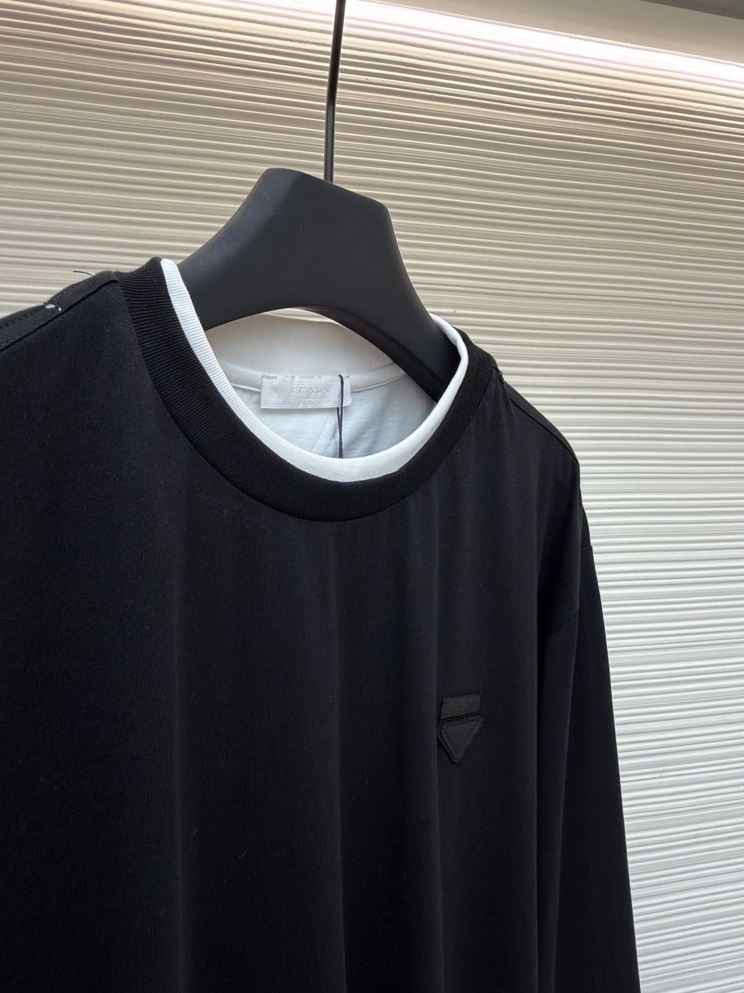 P140 Prada 三角标假两件长袖
●原版：6670购入开发
●货号：1680979-A20
●面料：精梳棉面料
●工艺：激光烧花制作
●版型：合身版型
●克重：约315克
●尺码：S-M-L
●描述：根据原版定制纱线，以达到特定的克重（200g/㎡）、厚度、韧性和手感。200克的重量确保了衣物具有良好的垂坠感和挺括度，不会轻飘也不会笨重。 “精梳” 工艺去除了棉纤维中的短绒和杂质，使得纱线更顺滑、强韧，织出的面料表面光洁、不易起球、触感细腻。“定染” 确保了颜色是专属且一致的，色彩饱和度与面料质感完美匹配，呈现出高级的单一色调。“假两件”设计是工艺智慧的体现。它并非简单地将两片布缝在一起，而是通过精密的一体化剪裁和拼接，模拟出两件衣物叠穿的层次效果。其复杂性在于无痕衔接：在领口、袖口和下摆处的拼接必须天衣无缝，模拟出内搭衣物的自然露出状态。这需要对不同面料的模拟拼接处进行特殊的滚边或压胶处理，使其边缘平整、过渡自然。整体走线平直细腻，面料舒适柔软，颜色一致无色差 能与同款搭配营造时尚造型，驾驭各种场合，定制辅料，三标齐全，男女同款！