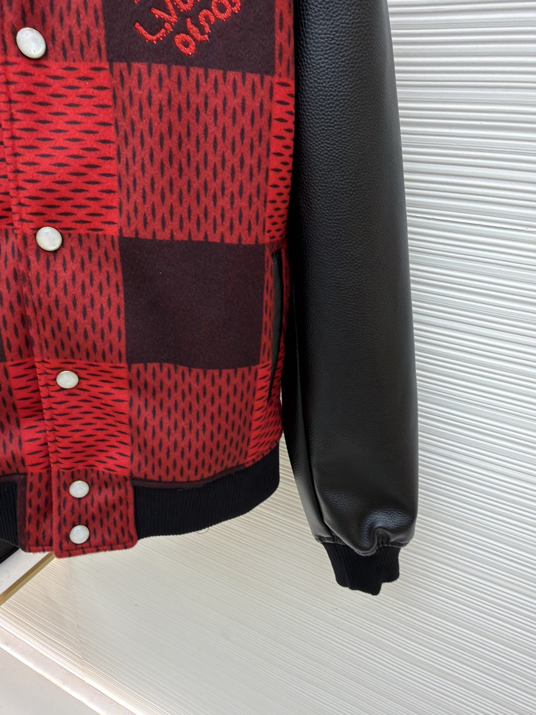 P330 LOUIS VUITTON 格纹Logo字母串珠刺绣夹克
●原版：45646购入开发
●货号：1681758-B95
●面料：羊毛混纺面料
●工艺：串珠刺绣制作
●颜色：红黑格子
●版型：合身版型
●克重：约1250克
●尺码：46-48-50-52
●描述：主体采用撞色格纹针织面料，通过提花编织工艺打造纹理层次，触感柔软且版型挺括；袖子拼接哑光皮革材质，经防刮耐磨处理，兼具质感与耐用性。衣身装饰品牌字母标识，采用立体绣线工艺，色彩鲜明且纹理清晰，强化辨识度。版型为合身棒球领设计，搭配珍珠纽扣开合，穿脱便捷；罗纹领口、袖口及下摆增强贴合度，兼顾防风性与休闲感。全衣拼接处采用精密锁边工艺，无外露线头，手工测量尺寸（误差1-3CM属正常），工艺平衡了针织的柔和与皮革的硬朗，呈现品牌潮流高级风格。整体走线平直细腻，面料舒适柔软，颜色一致无色差 能与同款搭配营造时尚造型，驾驭各种场合，定制辅料，三标齐全，男女同款！