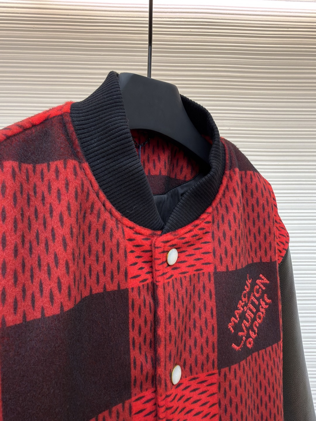 P330 LOUIS VUITTON 格纹Logo字母串珠刺绣夹克
●原版：45646购入开发
●货号：1681758-B95
●面料：羊毛混纺面料
●工艺：串珠刺绣制作
●颜色：红黑格子
●版型：合身版型
●克重：约1250克
●尺码：46-48-50-52
●描述：主体采用撞色格纹针织面料，通过提花编织工艺打造纹理层次，触感柔软且版型挺括；袖子拼接哑光皮革材质，经防刮耐磨处理，兼具质感与耐用性。衣身装饰品牌字母标识，采用立体绣线工艺，色彩鲜明且纹理清晰，强化辨识度。版型为合身棒球领设计，搭配珍珠纽扣开合，穿脱便捷；罗纹领口、袖口及下摆增强贴合度，兼顾防风性与休闲感。全衣拼接处采用精密锁边工艺，无外露线头，手工测量尺寸（误差1-3CM属正常），工艺平衡了针织的柔和与皮革的硬朗，呈现品牌潮流高级风格。整体走线平直细腻，面料舒适柔软，颜色一致无色差 能与同款搭配营造时尚造型，驾驭各种场合，定制辅料，三标齐全，男女同款！