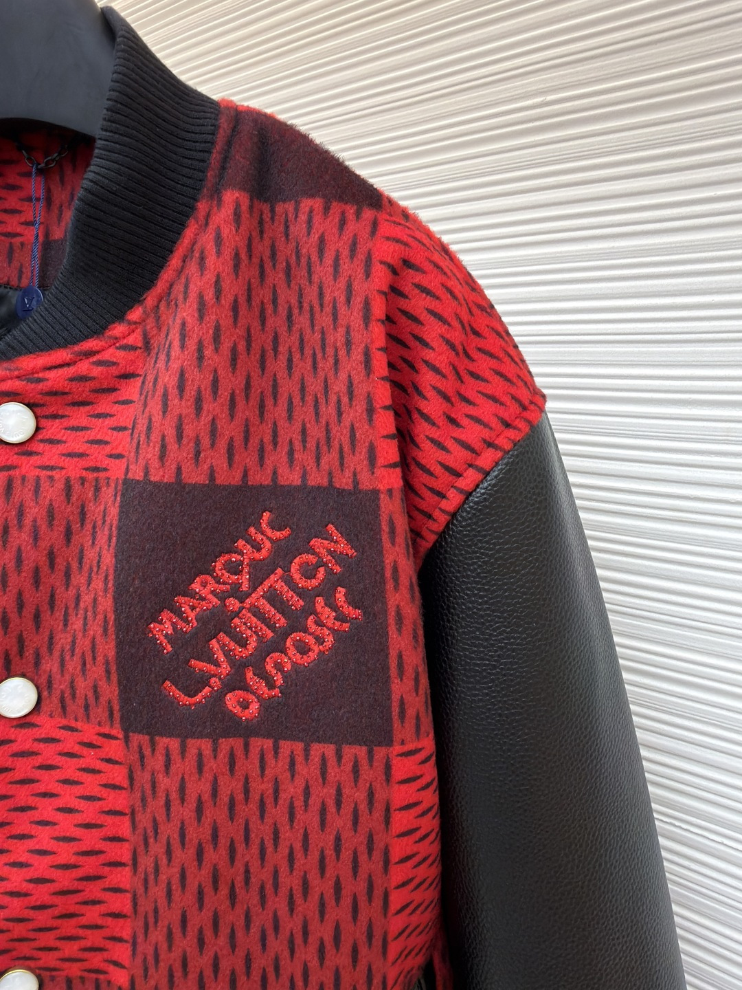P330 LOUIS VUITTON 格纹Logo字母串珠刺绣夹克
●原版：45646购入开发
●货号：1681758-B95
●面料：羊毛混纺面料
●工艺：串珠刺绣制作
●颜色：红黑格子
●版型：合身版型
●克重：约1250克
●尺码：46-48-50-52
●描述：主体采用撞色格纹针织面料，通过提花编织工艺打造纹理层次，触感柔软且版型挺括；袖子拼接哑光皮革材质，经防刮耐磨处理，兼具质感与耐用性。衣身装饰品牌字母标识，采用立体绣线工艺，色彩鲜明且纹理清晰，强化辨识度。版型为合身棒球领设计，搭配珍珠纽扣开合，穿脱便捷；罗纹领口、袖口及下摆增强贴合度，兼顾防风性与休闲感。全衣拼接处采用精密锁边工艺，无外露线头，手工测量尺寸（误差1-3CM属正常），工艺平衡了针织的柔和与皮革的硬朗，呈现品牌潮流高级风格。整体走线平直细腻，面料舒适柔软，颜色一致无色差 能与同款搭配营造时尚造型，驾驭各种场合，定制辅料，三标齐全，男女同款！