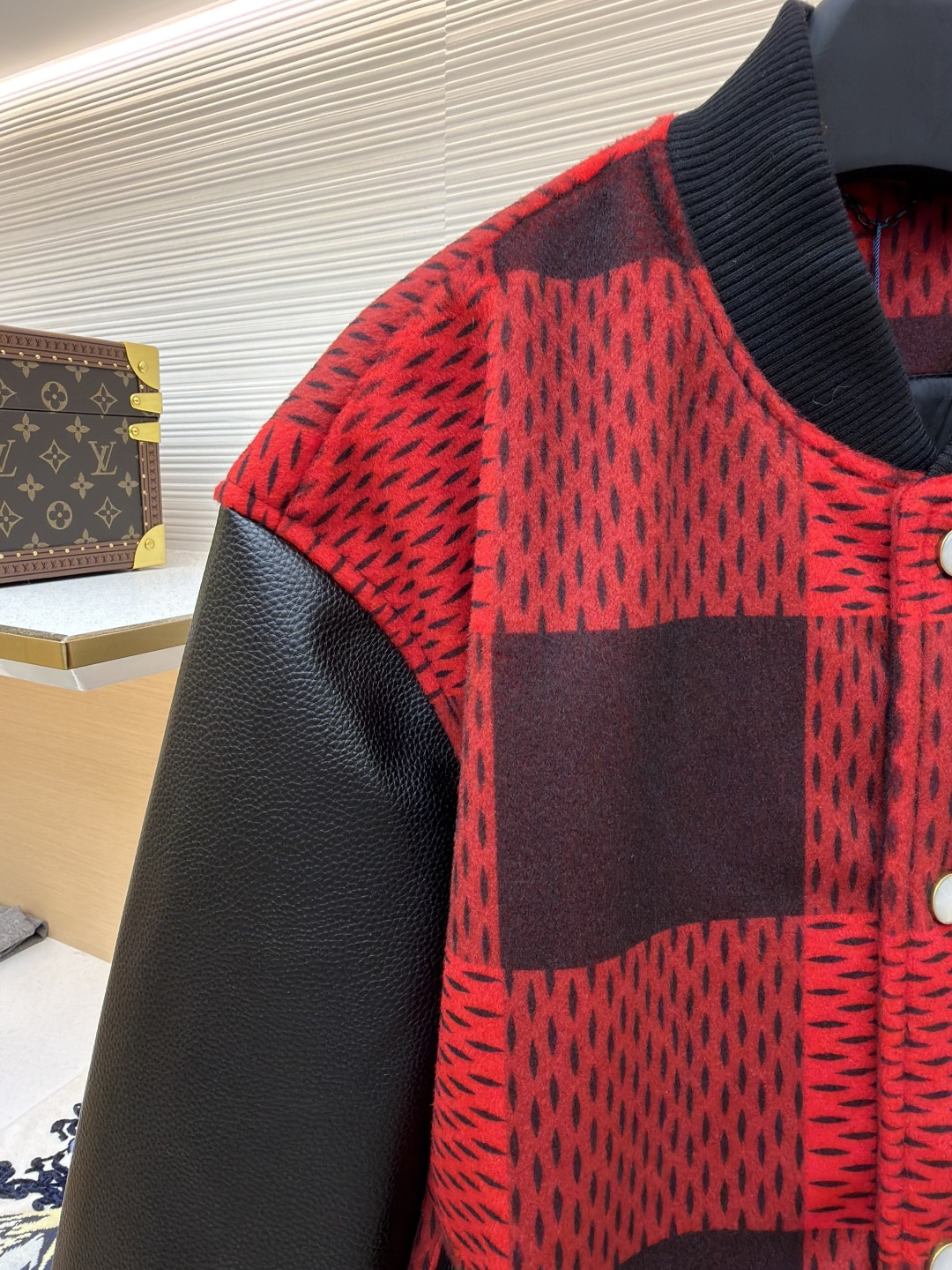 P330 LOUIS VUITTON 格纹Logo字母串珠刺绣夹克
●原版：45646购入开发
●货号：1681758-B95
●面料：羊毛混纺面料
●工艺：串珠刺绣制作
●颜色：红黑格子
●版型：合身版型
●克重：约1250克
●尺码：46-48-50-52
●描述：主体采用撞色格纹针织面料，通过提花编织工艺打造纹理层次，触感柔软且版型挺括；袖子拼接哑光皮革材质，经防刮耐磨处理，兼具质感与耐用性。衣身装饰品牌字母标识，采用立体绣线工艺，色彩鲜明且纹理清晰，强化辨识度。版型为合身棒球领设计，搭配珍珠纽扣开合，穿脱便捷；罗纹领口、袖口及下摆增强贴合度，兼顾防风性与休闲感。全衣拼接处采用精密锁边工艺，无外露线头，手工测量尺寸（误差1-3CM属正常），工艺平衡了针织的柔和与皮革的硬朗，呈现品牌潮流高级风格。整体走线平直细腻，面料舒适柔软，颜色一致无色差 能与同款搭配营造时尚造型，驾驭各种场合，定制辅料，三标齐全，男女同款！