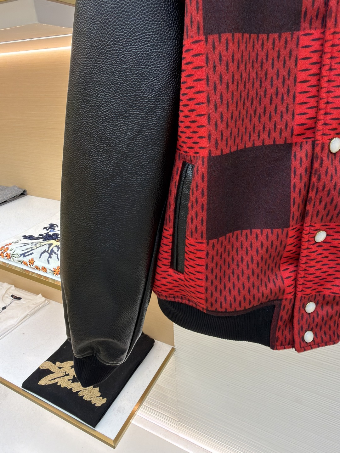 P330 LOUIS VUITTON 格纹Logo字母串珠刺绣夹克
●原版：45646购入开发
●货号：1681758-B95
●面料：羊毛混纺面料
●工艺：串珠刺绣制作
●颜色：红黑格子
●版型：合身版型
●克重：约1250克
●尺码：46-48-50-52
●描述：主体采用撞色格纹针织面料，通过提花编织工艺打造纹理层次，触感柔软且版型挺括；袖子拼接哑光皮革材质，经防刮耐磨处理，兼具质感与耐用性。衣身装饰品牌字母标识，采用立体绣线工艺，色彩鲜明且纹理清晰，强化辨识度。版型为合身棒球领设计，搭配珍珠纽扣开合，穿脱便捷；罗纹领口、袖口及下摆增强贴合度，兼顾防风性与休闲感。全衣拼接处采用精密锁边工艺，无外露线头，手工测量尺寸（误差1-3CM属正常），工艺平衡了针织的柔和与皮革的硬朗，呈现品牌潮流高级风格。整体走线平直细腻，面料舒适柔软，颜色一致无色差 能与同款搭配营造时尚造型，驾驭各种场合，定制辅料，三标齐全，男女同款！