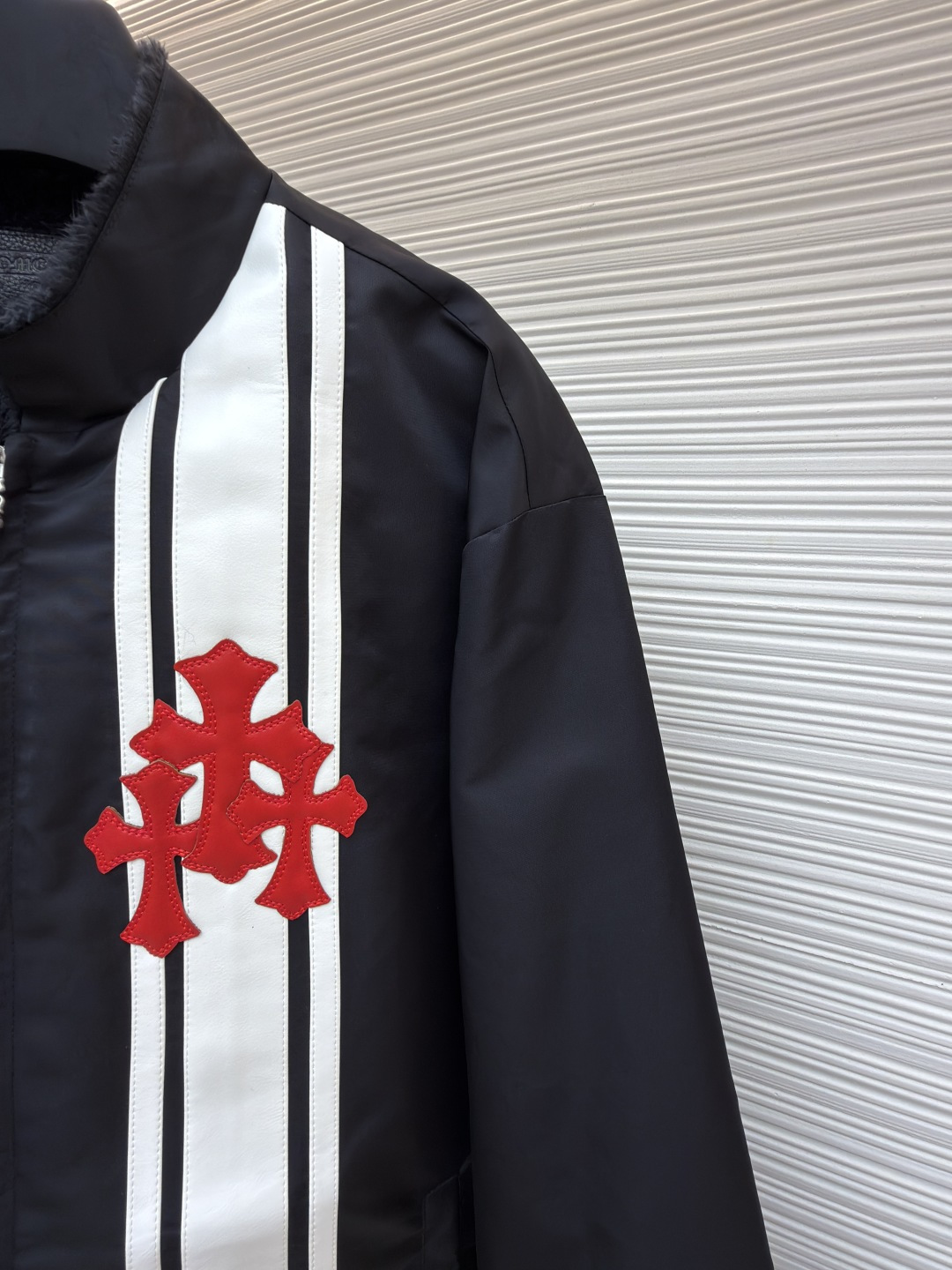 P295 Chrome Hearts 贴布条纹夹克
●原版：30000购入开发
●货号：1681765-B60
●面料：聚酯纤维面料
●工艺：贴布制作
●颜色：黑色
●版型：合身版型
●克重：约680克
●尺码：S-M-L-XL
●描述：采用高密防风面料，经防泼水涂层处理，兼具耐用性与防护性，触感顺滑且不易起皱。衣身侧边拼接黑白条纹装饰，通过精准定位缝制工艺固定，线条规整增强视觉层次；正面装饰品牌红色Logo印花，采用高温烫印工艺，色彩饱和且不易脱落，凸显辨识度。版型为宽松剪裁，搭配金属拉链开合，穿脱便捷；罗纹领口、袖口及下摆增强贴合度，兼顾防风性与休闲感。全衣缝线工整，拼接处无外露线头，手工测量尺寸（误差1-3CM属正常），工艺平衡了街头风格与品牌标志性设计，是兼具实穿性与潮流感的单品。整体走线平直细腻，面料舒适柔软，颜色一致无色差 能与同款搭配营造时尚造型，驾驭各种场合，定制辅料，三标齐全，男女同款！