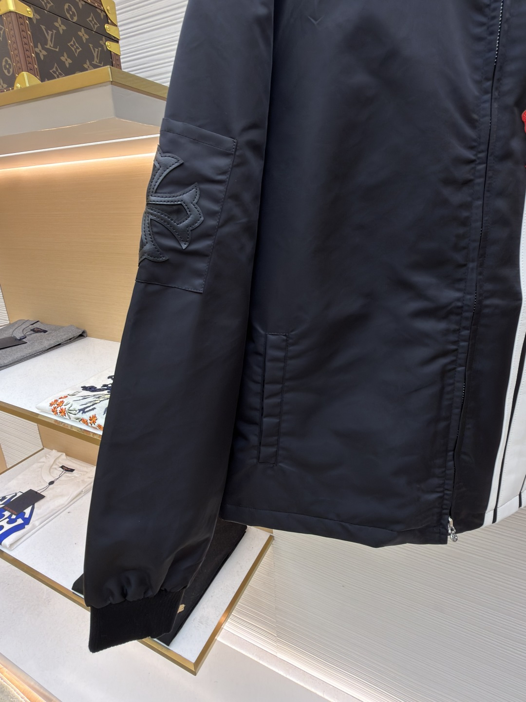 P295 Chrome Hearts 贴布条纹夹克
●原版：30000购入开发
●货号：1681765-B60
●面料：聚酯纤维面料
●工艺：贴布制作
●颜色：黑色
●版型：合身版型
●克重：约680克
●尺码：S-M-L-XL
●描述：采用高密防风面料，经防泼水涂层处理，兼具耐用性与防护性，触感顺滑且不易起皱。衣身侧边拼接黑白条纹装饰，通过精准定位缝制工艺固定，线条规整增强视觉层次；正面装饰品牌红色Logo印花，采用高温烫印工艺，色彩饱和且不易脱落，凸显辨识度。版型为宽松剪裁，搭配金属拉链开合，穿脱便捷；罗纹领口、袖口及下摆增强贴合度，兼顾防风性与休闲感。全衣缝线工整，拼接处无外露线头，手工测量尺寸（误差1-3CM属正常），工艺平衡了街头风格与品牌标志性设计，是兼具实穿性与潮流感的单品。整体走线平直细腻，面料舒适柔软，颜色一致无色差 能与同款搭配营造时尚造型，驾驭各种场合，定制辅料，三标齐全，男女同款！