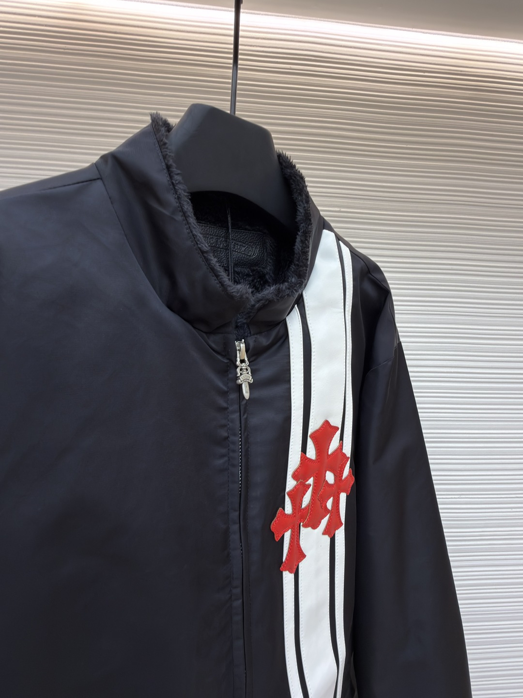 P295 Chrome Hearts 贴布条纹夹克
●原版：30000购入开发
●货号：1681765-B60
●面料：聚酯纤维面料
●工艺：贴布制作
●颜色：黑色
●版型：合身版型
●克重：约680克
●尺码：S-M-L-XL
●描述：采用高密防风面料，经防泼水涂层处理，兼具耐用性与防护性，触感顺滑且不易起皱。衣身侧边拼接黑白条纹装饰，通过精准定位缝制工艺固定，线条规整增强视觉层次；正面装饰品牌红色Logo印花，采用高温烫印工艺，色彩饱和且不易脱落，凸显辨识度。版型为宽松剪裁，搭配金属拉链开合，穿脱便捷；罗纹领口、袖口及下摆增强贴合度，兼顾防风性与休闲感。全衣缝线工整，拼接处无外露线头，手工测量尺寸（误差1-3CM属正常），工艺平衡了街头风格与品牌标志性设计，是兼具实穿性与潮流感的单品。整体走线平直细腻，面料舒适柔软，颜色一致无色差 能与同款搭配营造时尚造型，驾驭各种场合，定制辅料，三标齐全，男女同款！