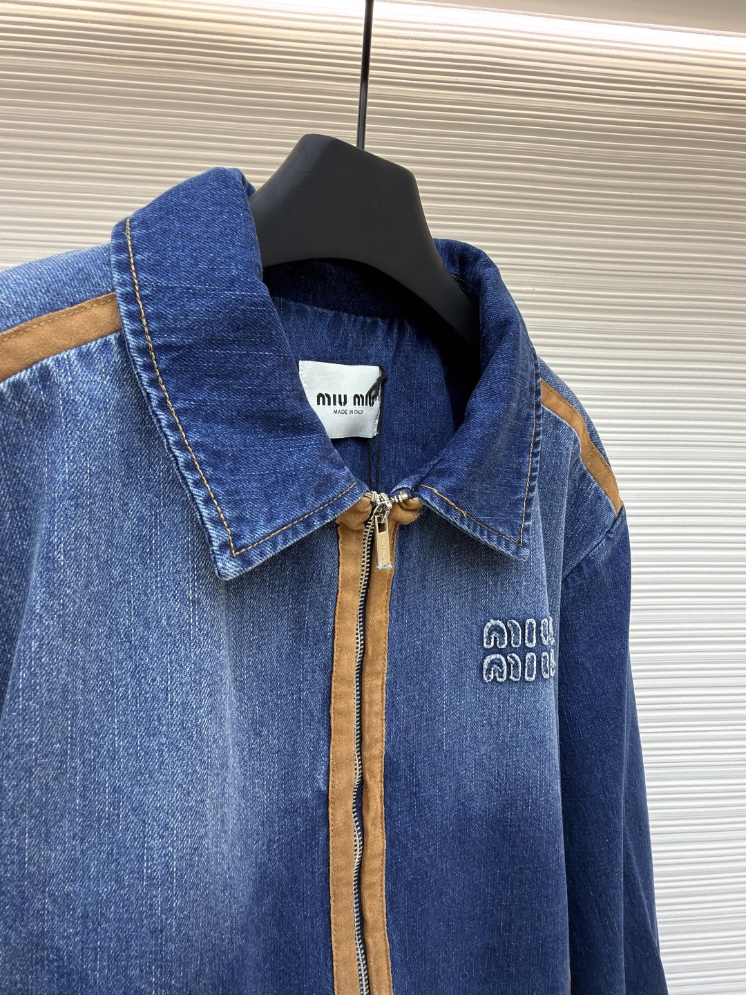 P280 MIU MIU皮革饰边牛仔外套 
●原版：16708购入开发
●货号：1681771-B45
●面料：牛仔面料
●工艺：立体绣线制作
●颜色：蓝色
●版型：合身版型
●克重：约1085克
●尺码：S-M-L
●描述：采用做旧水洗牛仔面料，经石磨工艺处理，呈现自然渐变色泽，触感柔软且保留牛仔挺括质感。衣身拼接棕褐色皮质饰条，通过精密车缝工艺固定，纹理细腻增强复古层次；胸前装饰品牌字母刺绣，采用立体绣线工艺，线条清晰且不易脱落，凸显辨识度。版型为宽松剪裁，适配多元身形，拉链开合搭配翻领设计，穿脱便捷且适配多场景；袖口、下摆采用牛仔原边收缝，保障版型利落度。全衣缝线工整，拼接处无外露线头，手工测量尺寸（误差1-3CM属正常），工艺平衡了复古牛仔与甜酷风格，是兼具实穿性与造型感的单品。整体走线平直细腻，面料舒适柔软，颜色一致无色差 能与同款搭配营造时尚造型，驾驭各种场合，定制辅料，三标齐全，男女同款！