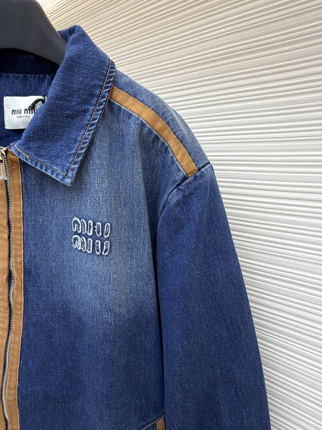 P280 MIU MIU皮革饰边牛仔外套 
●原版：16708购入开发
●货号：1681771-B45
●面料：牛仔面料
●工艺：立体绣线制作
●颜色：蓝色
●版型：合身版型
●克重：约1085克
●尺码：S-M-L
●描述：采用做旧水洗牛仔面料，经石磨工艺处理，呈现自然渐变色泽，触感柔软且保留牛仔挺括质感。衣身拼接棕褐色皮质饰条，通过精密车缝工艺固定，纹理细腻增强复古层次；胸前装饰品牌字母刺绣，采用立体绣线工艺，线条清晰且不易脱落，凸显辨识度。版型为宽松剪裁，适配多元身形，拉链开合搭配翻领设计，穿脱便捷且适配多场景；袖口、下摆采用牛仔原边收缝，保障版型利落度。全衣缝线工整，拼接处无外露线头，手工测量尺寸（误差1-3CM属正常），工艺平衡了复古牛仔与甜酷风格，是兼具实穿性与造型感的单品。整体走线平直细腻，面料舒适柔软，颜色一致无色差 能与同款搭配营造时尚造型，驾驭各种场合，定制辅料，三标齐全，男女同款！