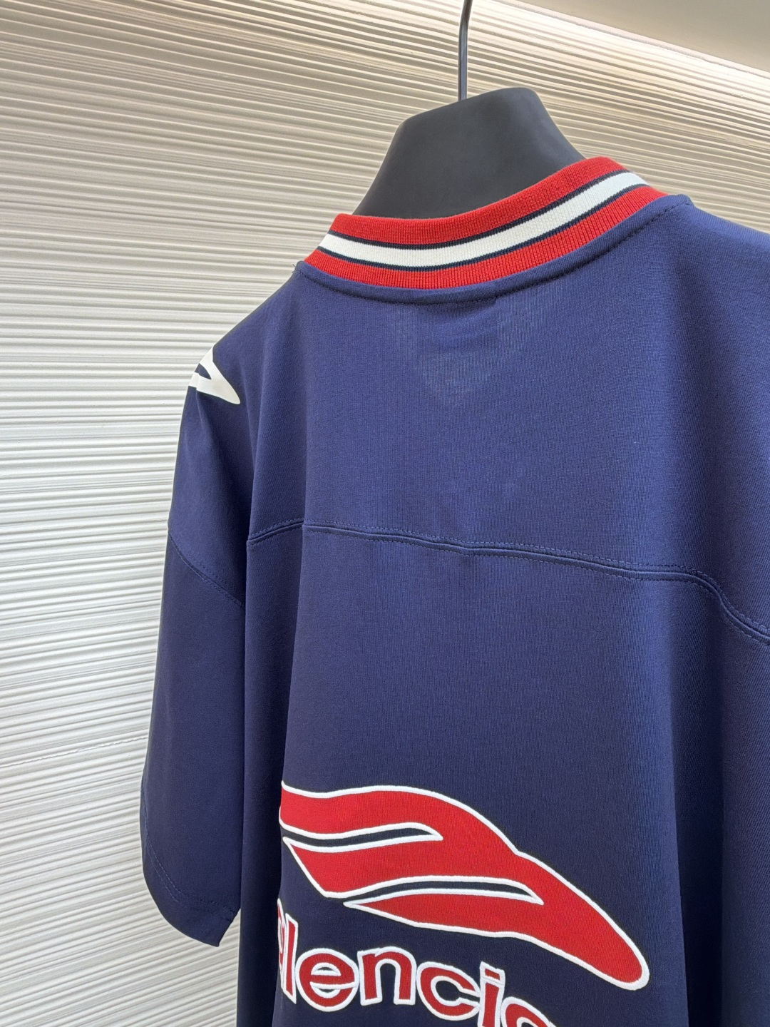 P180 Balenciaga 球队系列V领长袖
●原版：5699购入开发
●货号：1682041-A50
●面料：平纹针织紧密棉面料
●工艺：胶浆印花制作
●颜色：蓝色
●版型：宽松版型
●克重：约300克
●尺码：XS-S-M-L
●描述：主体采用24支特纺紧密棉，克重为185g/㎡。在纺纱环节应用了紧密纺技术，显著减少了纱线毛羽，使得纱线更光滑、强韧。这赋予了面料结构异常密实、表面光洁平整、抗起球性优异的特点，同时保留了纯棉的柔软透气性。185g的克重属于轻至中量级，确保了衣物轻盈、垂坠且活动自如的特性，非常适合打造兼具运动感与日常舒适度的长袖衫。V领部分由两种不同颜色的高弹罗纹面料拼接而成。其工艺步骤是先分别织造出两种颜色的罗纹带，再通过精准的剪裁与拼接，形成具有鲜明色彩对比的V形领口。打破了纯色衣身的单调，以强烈的色彩对比塑造出年轻、活力的视觉焦点，并优化了颈部线。将图案在不同材质或颜色的布料上预先裁剪成型贴布，然后将其覆盖在衣身上，最后用高密度绣线锁边固定并勾勒内部细节。其作用在于：创造色彩鲜明、质感对比强烈且极具立体感和耐用性的图案，图案边缘牢固，不易磨损。将特制的弹性浆料通过网版印刷在袖部的工艺，色彩鲜艳且具有轻微涂层感的图案。弹力浆料保证了印花区域能随面料一起拉伸而不开裂。与贴布绣的立体感形成一平一凸的质感对比，增加了设计的趣味性和复杂度。整体走线平直细腻，面料舒适柔软，颜色一致无色差 能与同款搭配营造时尚造型，驾驭各种场合，定制辅料，三标齐全，男女同款！